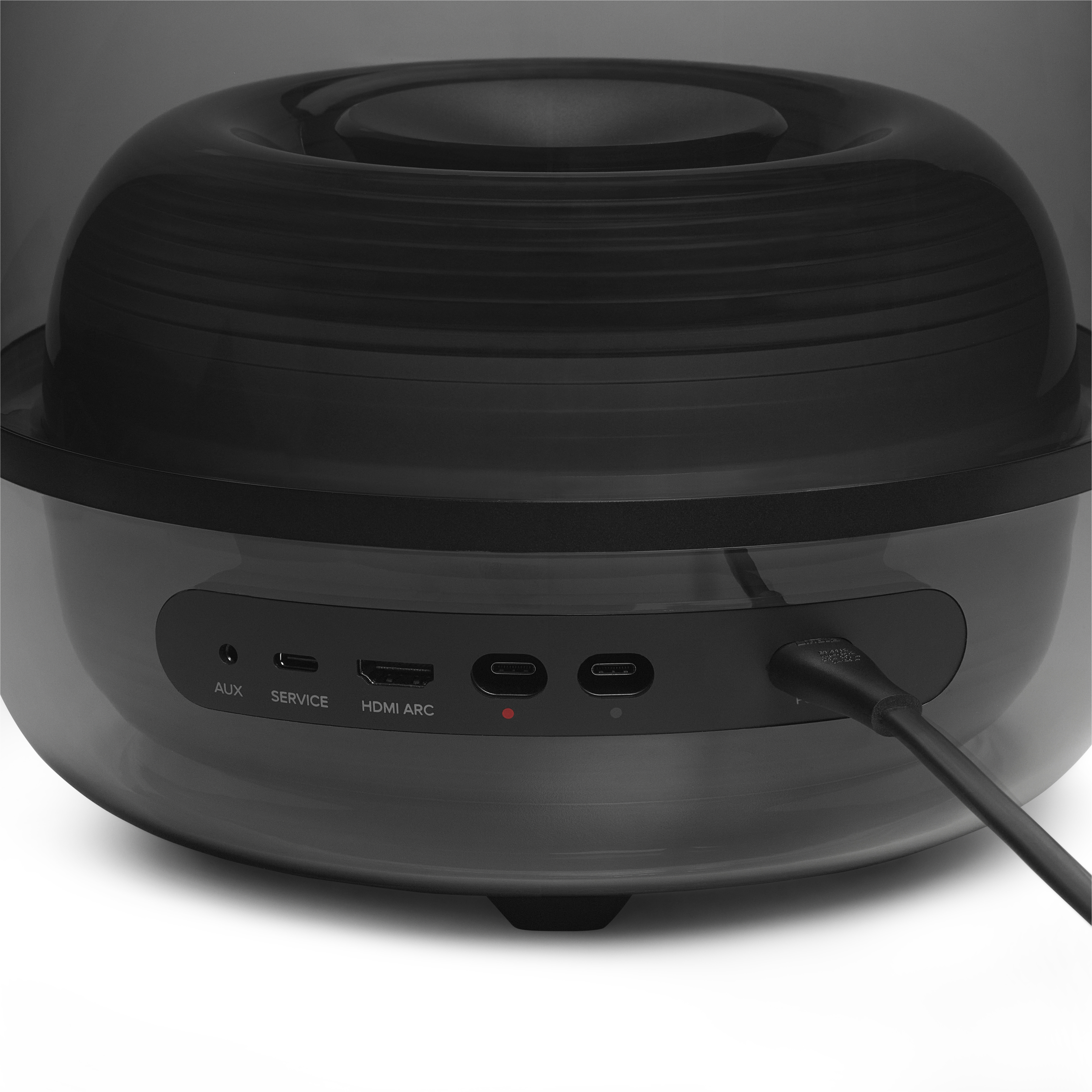 Schwarzes Audiogerät mit Anschlüssen und einem Netzkabel. Ein rotes Licht leuchtet. Das Gerät steht auf weißem Untergrund.