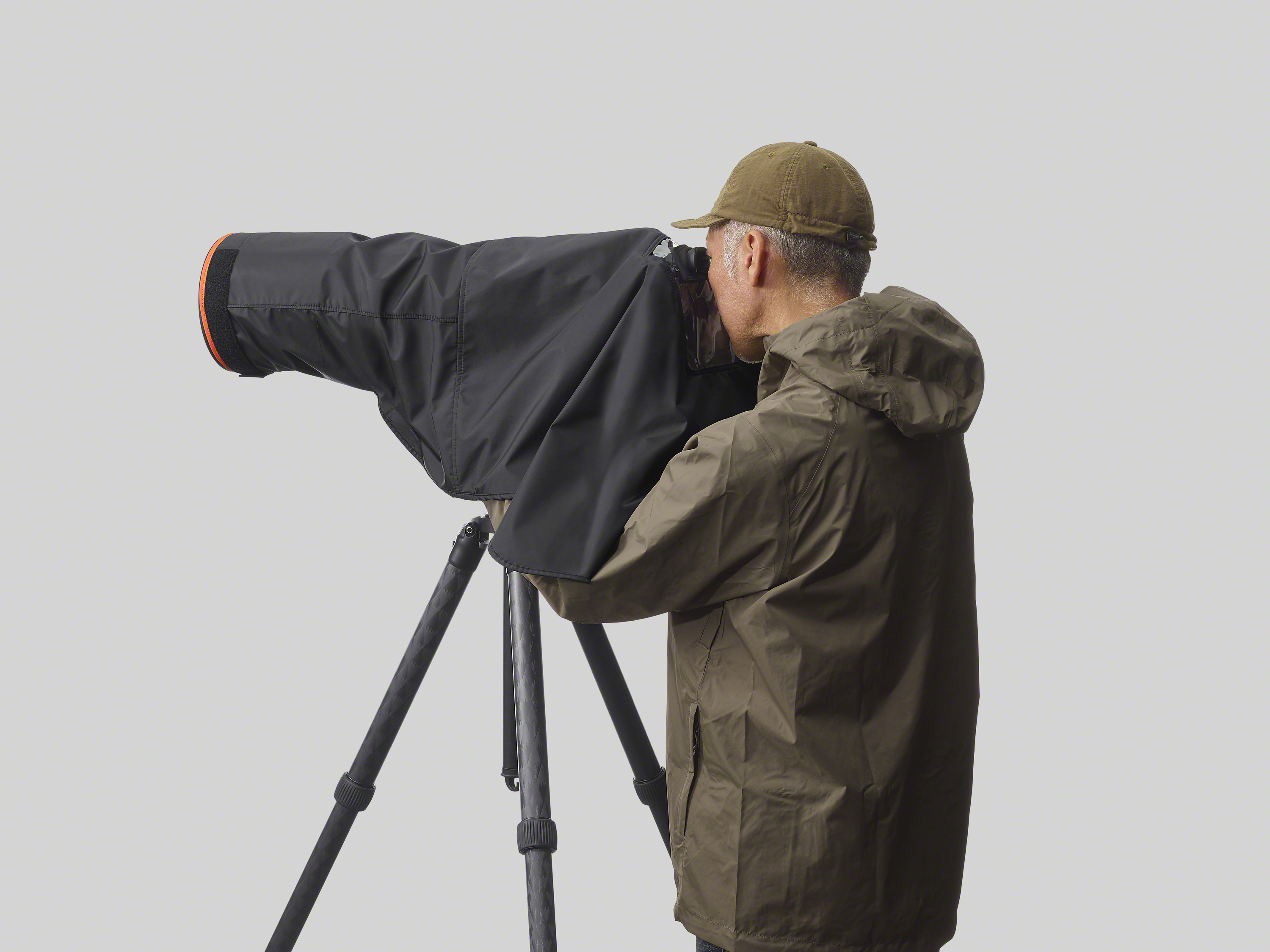 Un uomo con giacca e berretto guarda attraverso una fotocamera coperta su un treppiede. Lo sfondo è grigio.