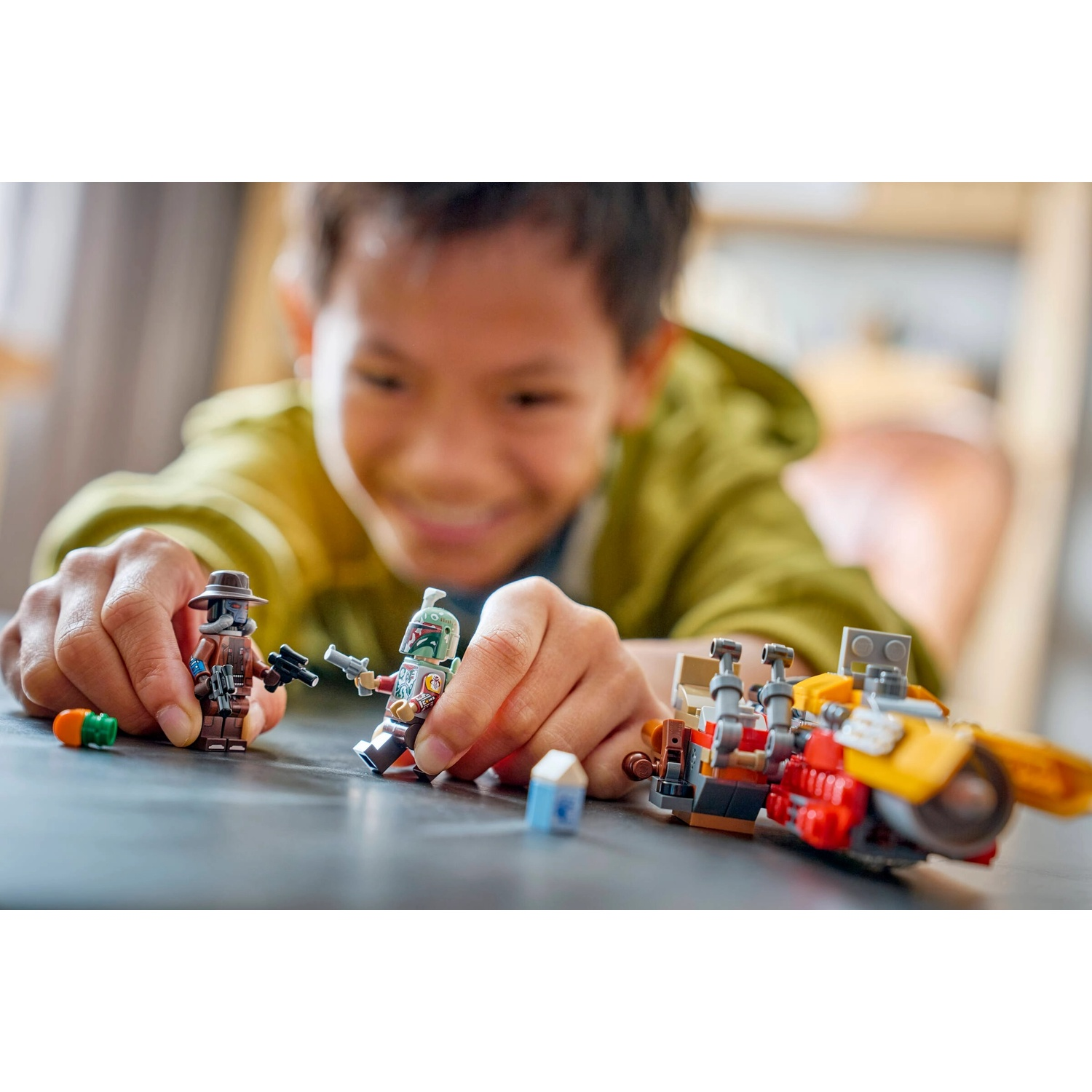 Un bambino gioca con i personaggi di Lego Star Wars e un veicolo su un tavolo. Il bambino sorride. Si tiene una pistola giocattolo.