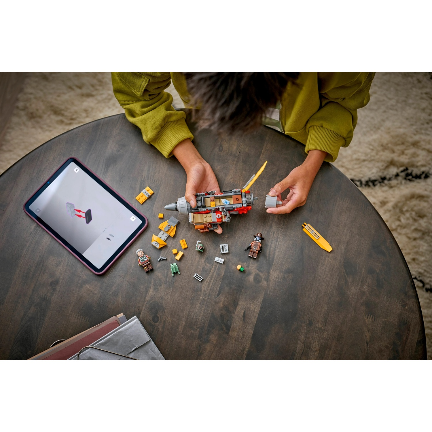 Una persona assembla un set Lego su un tavolo di legno. C'è un tablet con istruzioni, pezzi sparsi e personaggi Lego.