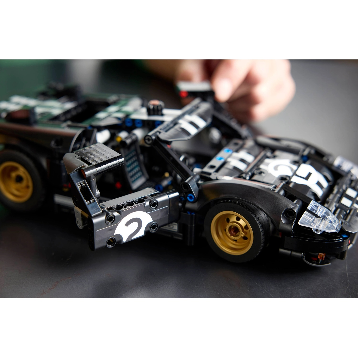 Un'auto sportiva Lego nera con ruote dorate, la portiera aperta, una mano sopra. L'auto ha il numero 2 sulla portiera.