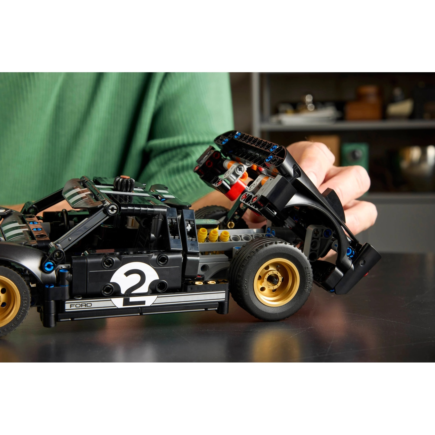Un'auto modello Lego Ford GT nera con ruote dorate, il cofano è aperto. Si vede la mano di una persona.