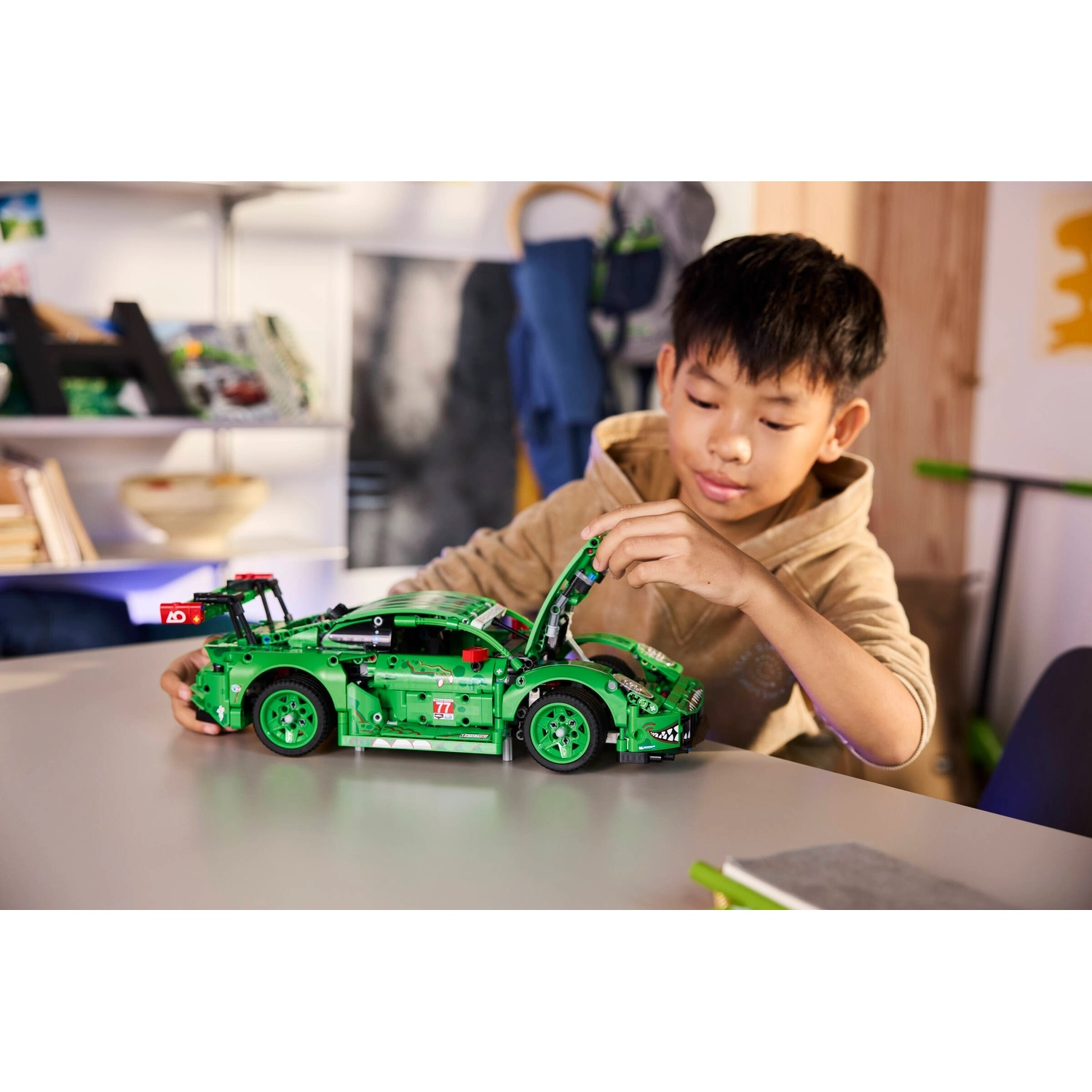 Un ragazzino sta costruendo una macchina da corsa Lego verde. Sta aprendo il cofano. L'auto è su un tavolo grigio.