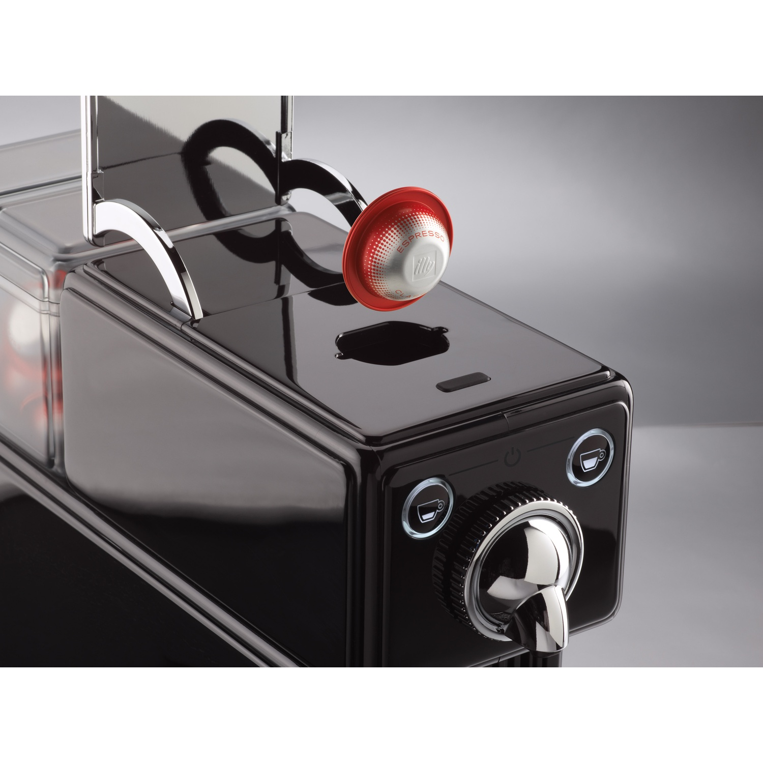 Una macchina per caffè espresso nera con una capsula rossa e argento sopra. Caratteristiche: beccuccio argentato e quadrante di controllo con icone di tazza illuminate.