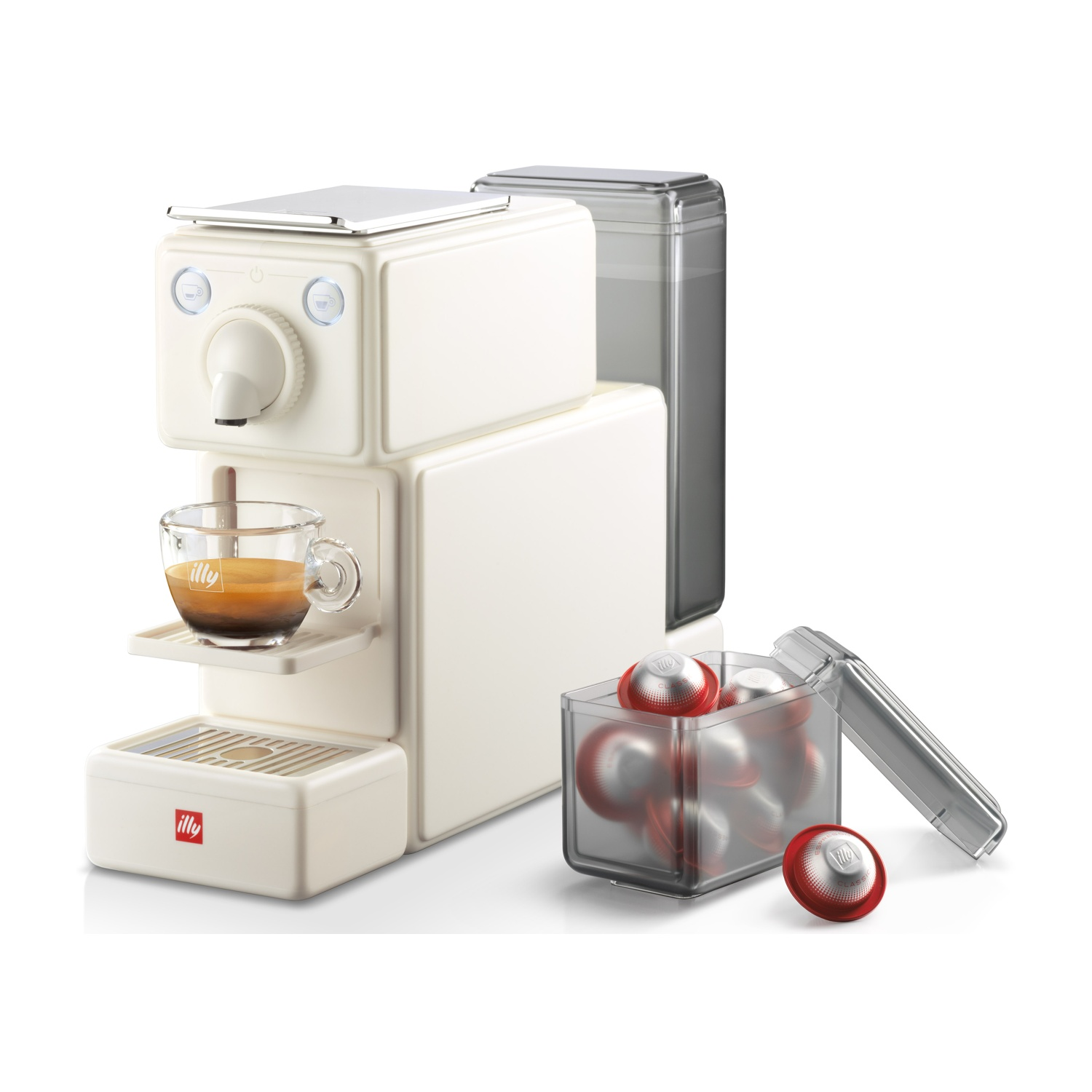 Una macchina per espresso Illy bianco sporco. Una tazza di vetro con caffè è sulla macchina. Capsule e un contenitore trasparente sono accanto.