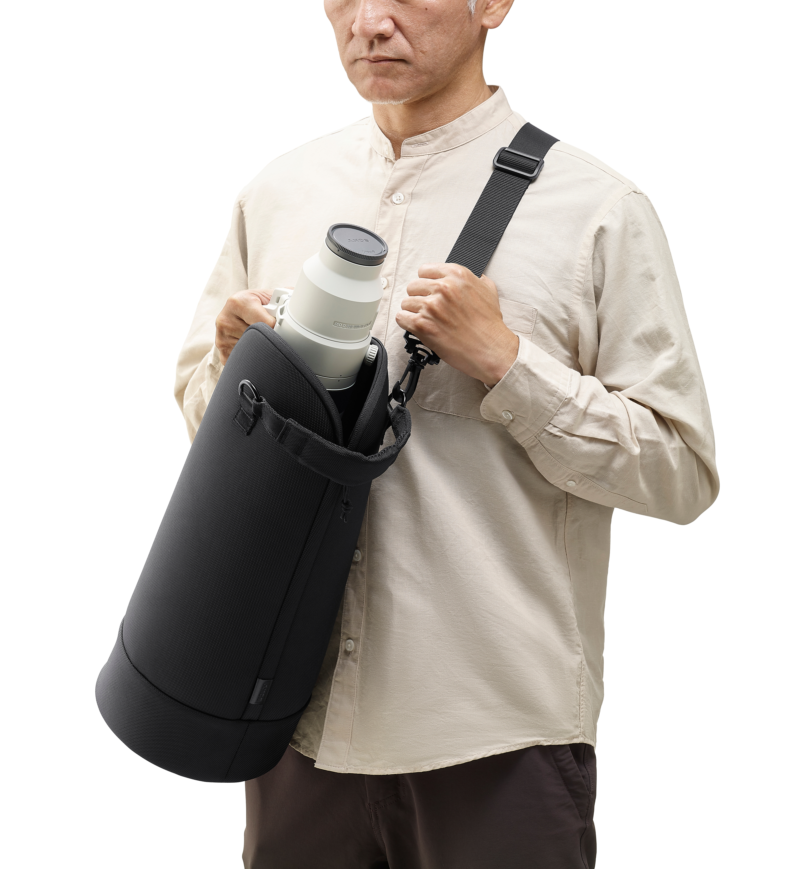 Un uomo tiene un obiettivo della fotocamera in una borsa nera, indossa una camicia chiara. Il cinturino è nero.