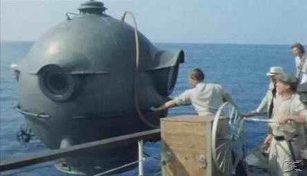 Ein rundes u-bootähnliches Objekt, Menschen auf einem Schiff und der Ozean im Hintergrund. Eine Person berührt das Objekt.