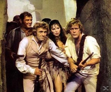 Vier Personen, zwei Männer halten Gewehre, eine Frau. Sie stehen in der Nähe einer Steinmauer. Die Szene wirkt wie aus einem Film.