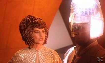 Eine Frau in einem goldenen Outfit und ein Mann mit einem leuchtenden Helm stehen vor einem orangefarbenen Hintergrund.