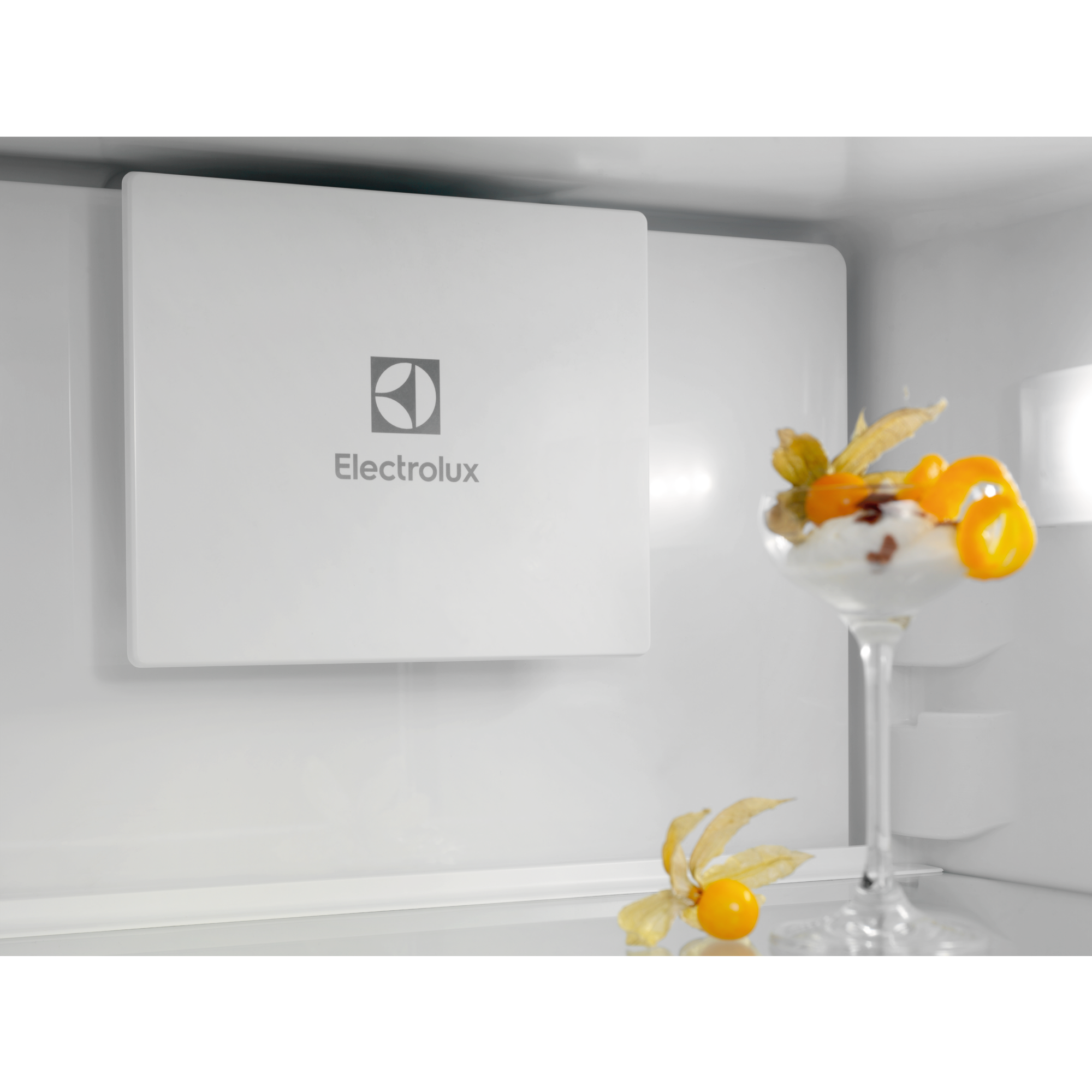 Wewnątrz lodówki deser z pomarańczowymi owocami. Po lewej panel Electrolux.