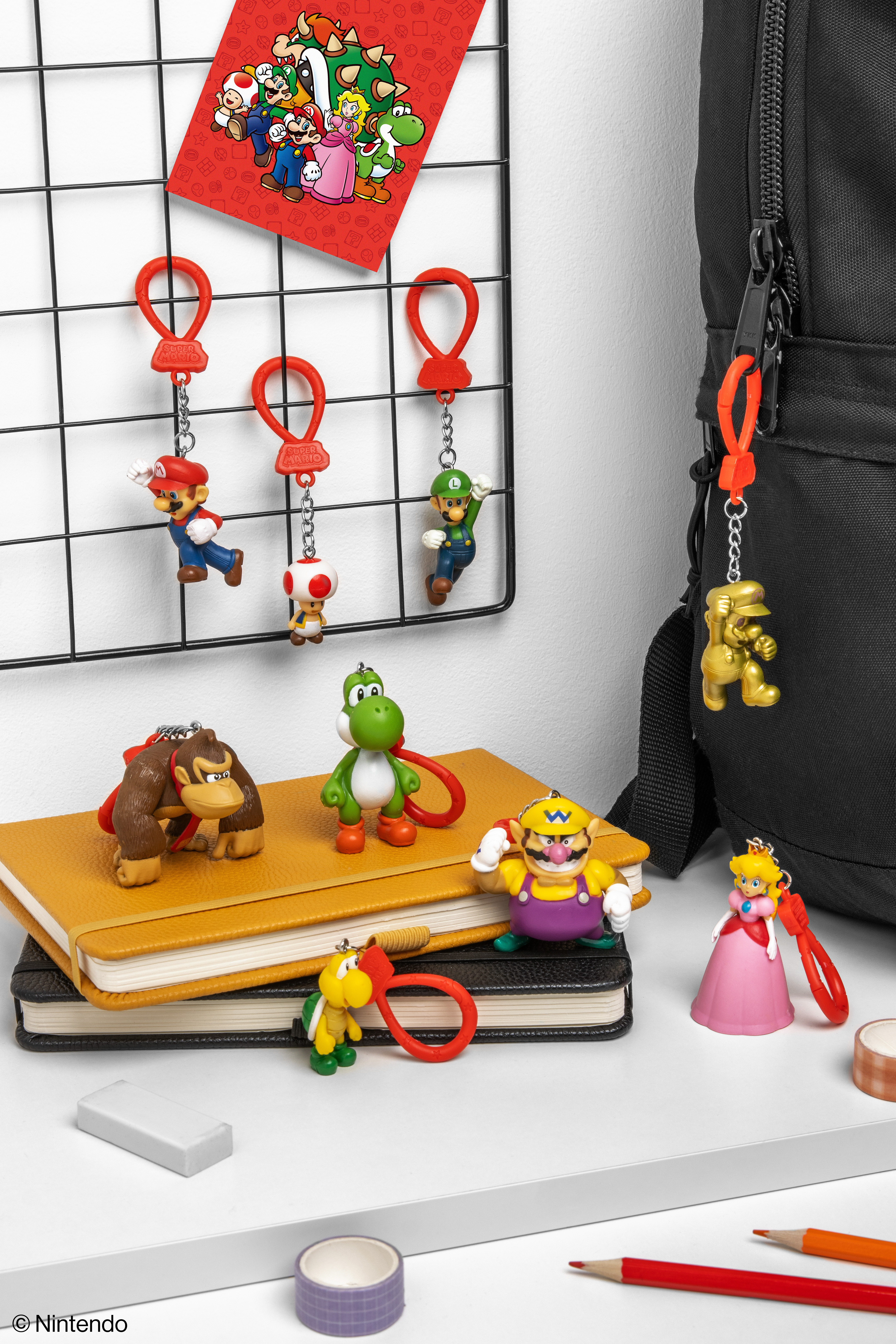 Verschiedene Super Mario-Figuren und ein rotes Poster. Auf der rechten Seite ein schwarzer Rucksack. Gelbe und schwarze Notizbücher links.