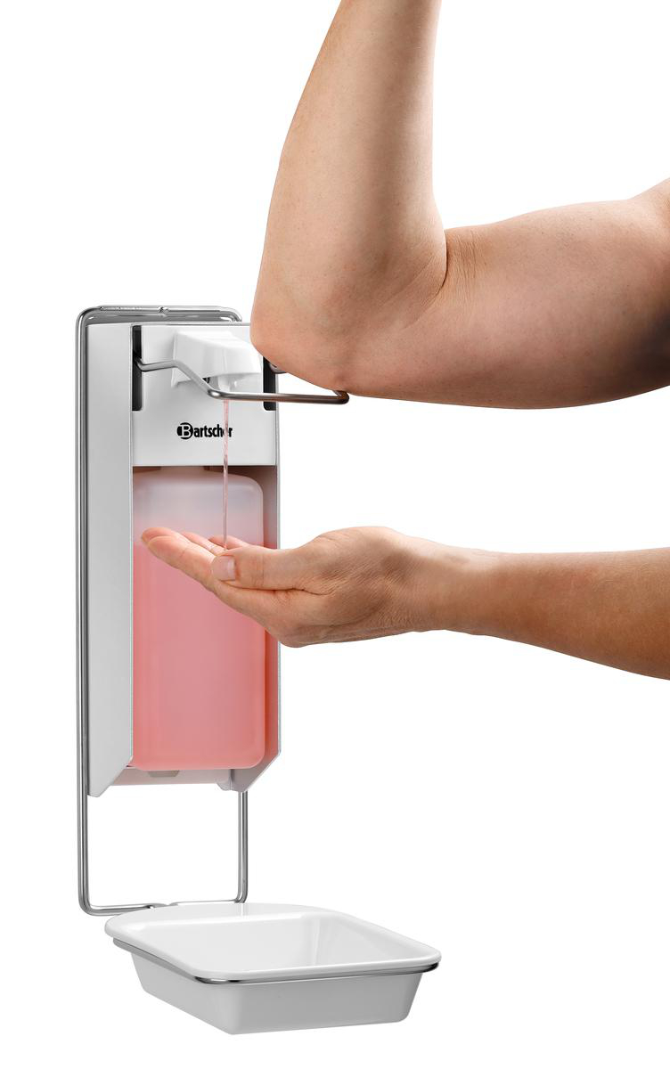 Eine Person benutzt einen Ellbogen, um rosa Seife aus einem Wandspender in ihre Hand zu geben. Darunter befindet sich ein weißes Becken.