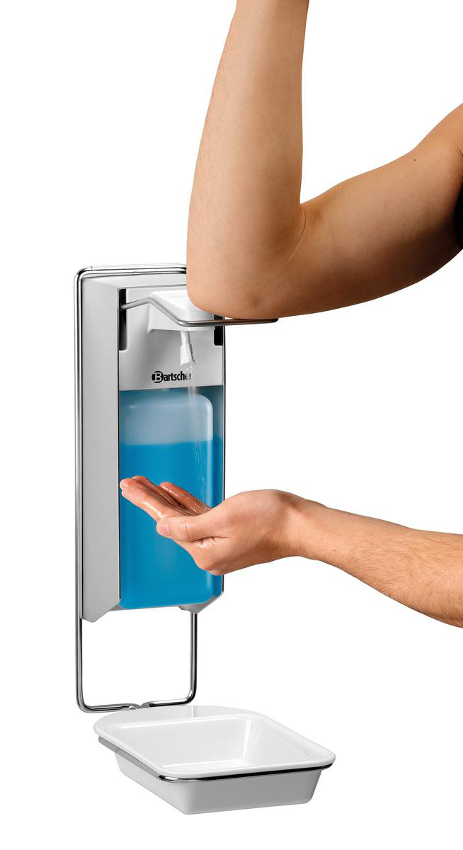 Eine Person benutzt den Ellbogen, um blaue Seife aus einem Wandspender in ihre Hand zu geben, über einer weißen Schale.
