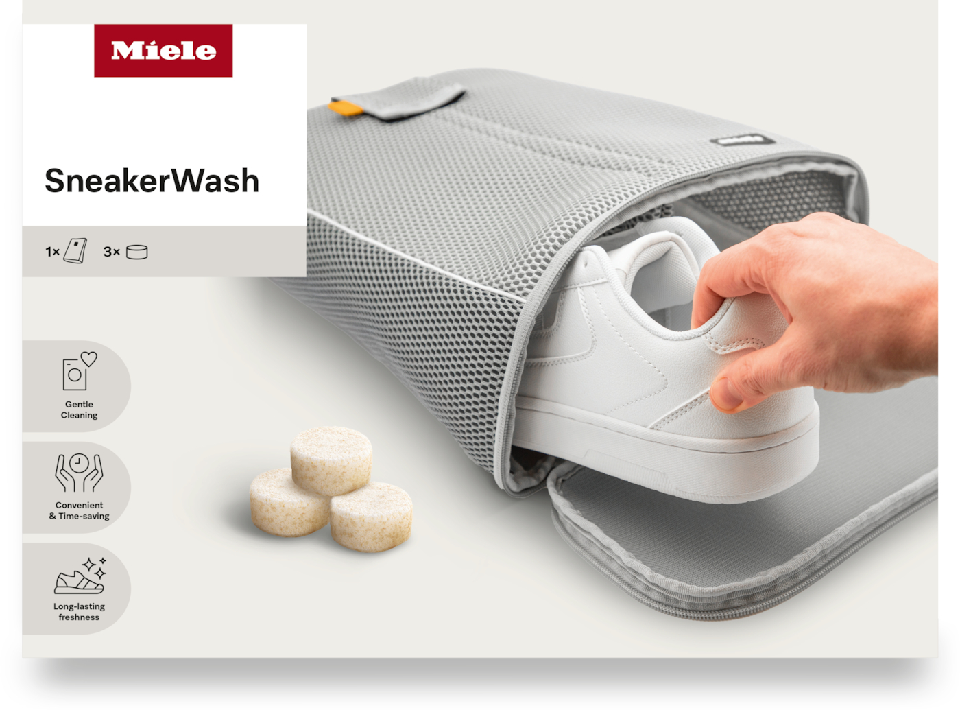 Ein weißer Sneaker wird in eine graue Netztasche gelegt. Drei Reinigungstabletten sind vorne. Das Miele-Logo und der Text SneakerWash sind sichtbar.