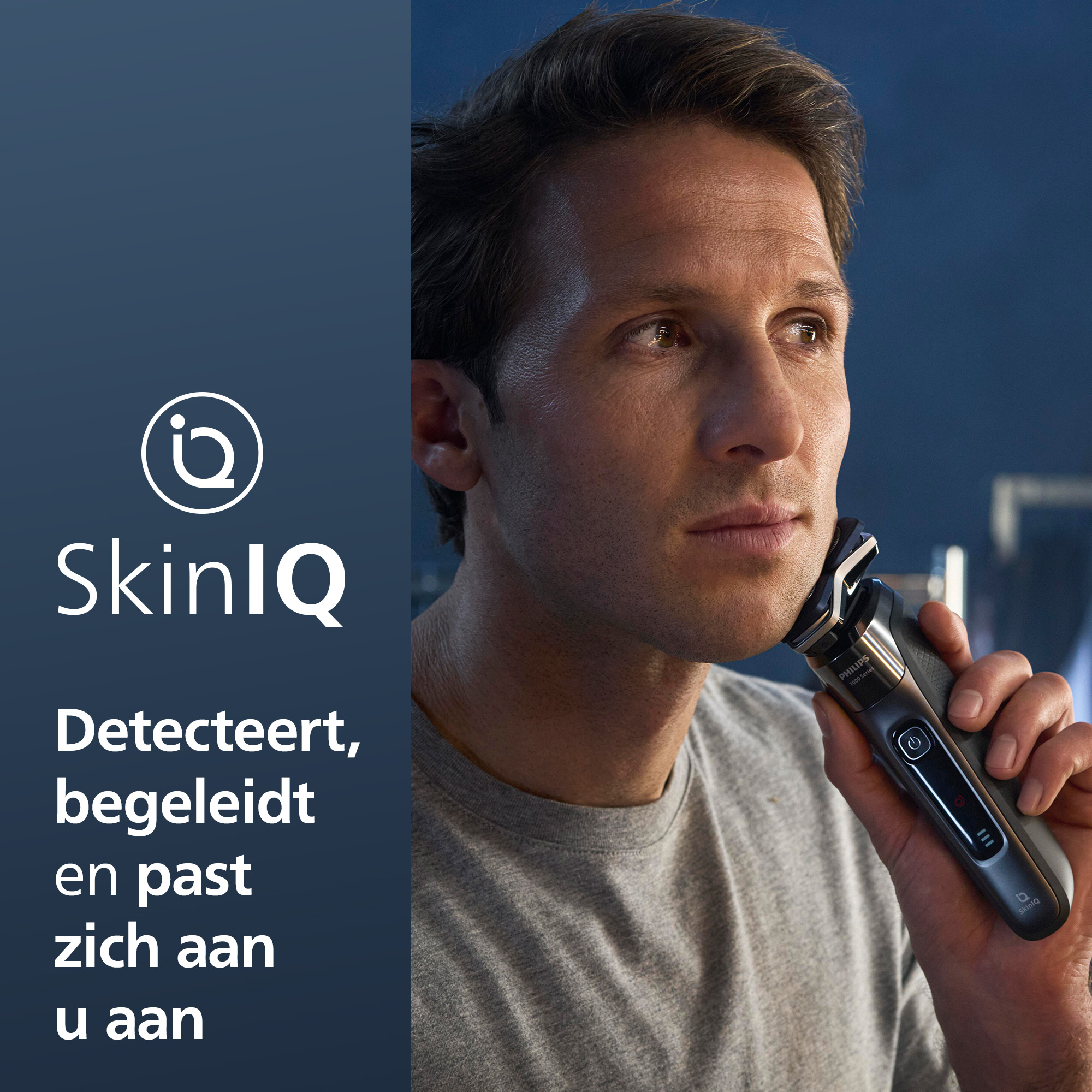 A man shaves with a Philips shaver. The shaver is black and silver, and the man is wearing a gray shirt.
