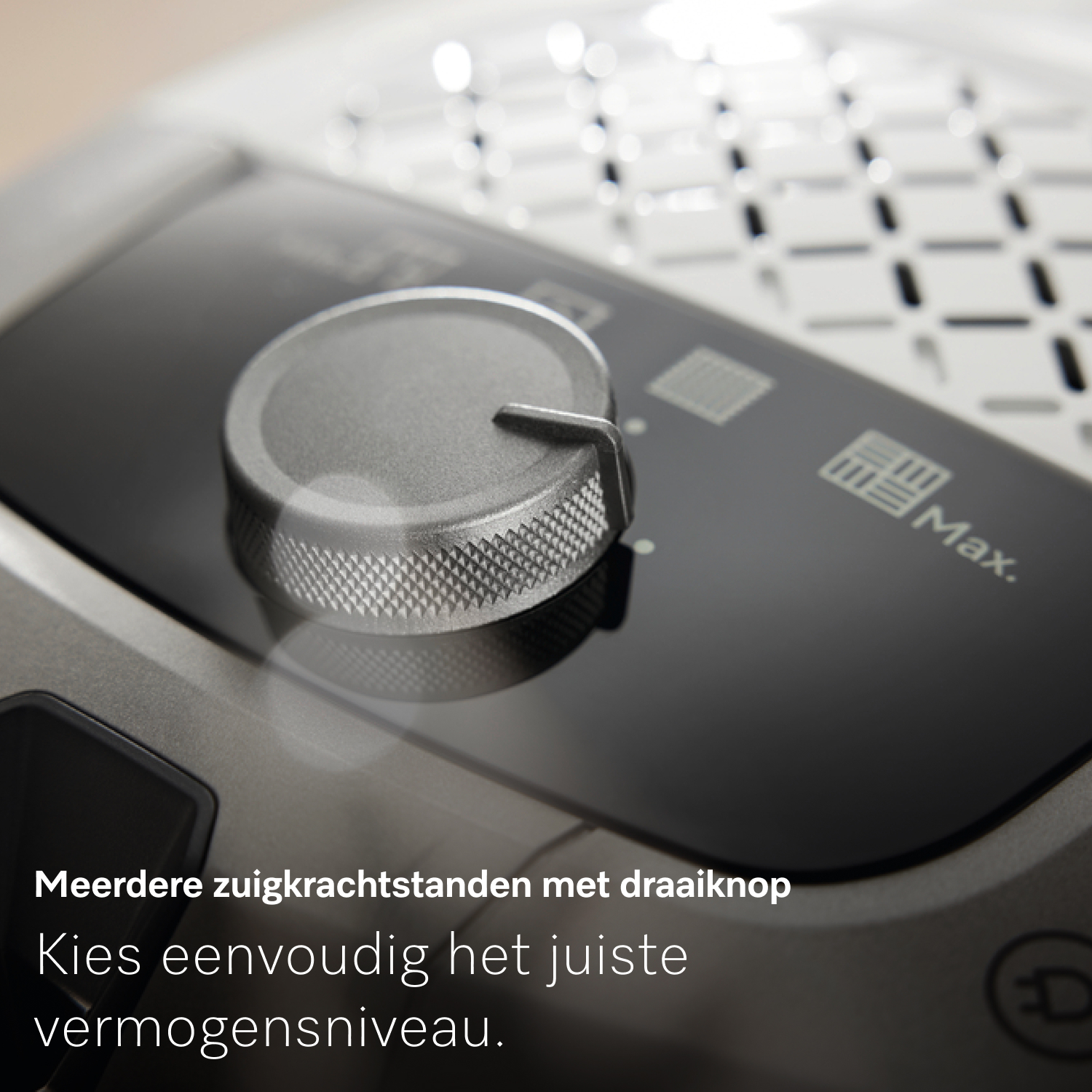 Close-up van het bedieningspaneel van een stofzuiger. Een zilveren draaiknop op een zwart oppervlak. Het woord 'Max' is zichtbaar. De knop past de kracht aan.