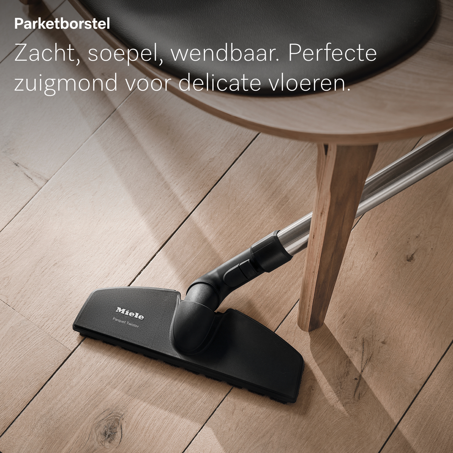 Zwarte Miele stofzuigerkop op een houten vloer, onder een stoel. De vloer is lichtbruin. De stofzuiger is 'Parquet Twister'.