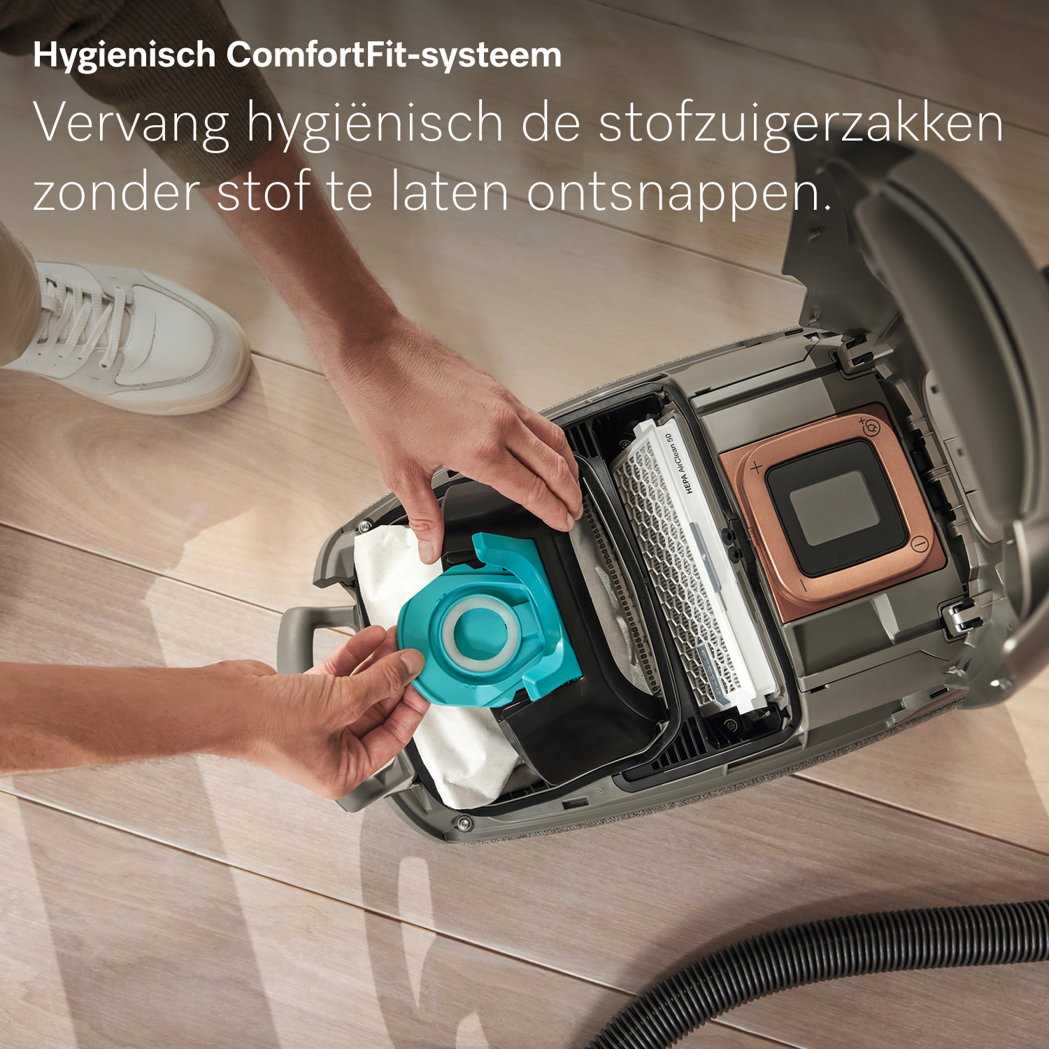 A person replaces a vacuum cleaner bag. The vacuum cleaner is open. The new bag is turquoise. The background is wooden floor.