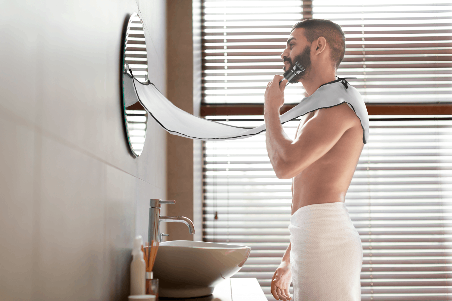 Un hombre se afeita la barba en un baño. Está sin camisa, envuelto en una toalla. Un espejo y persianas en el fondo.