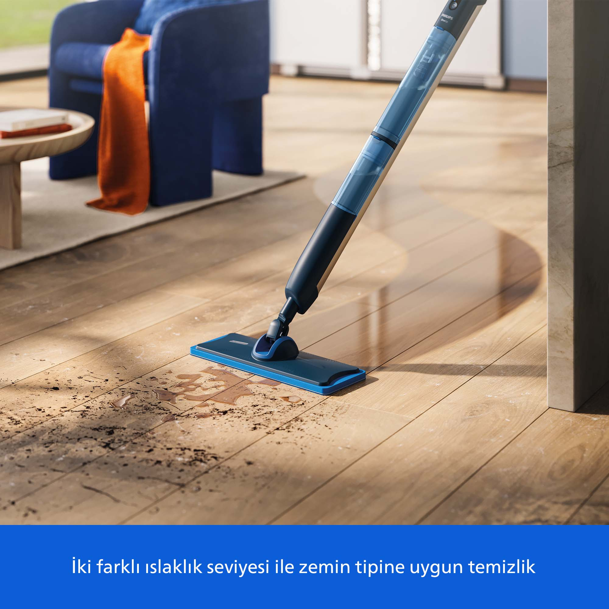 Mavi ve siyah bir paspas ahşap bir zemini temizliyor. Arka planda mavi bir sandalye ve turuncu bir battaniye var.