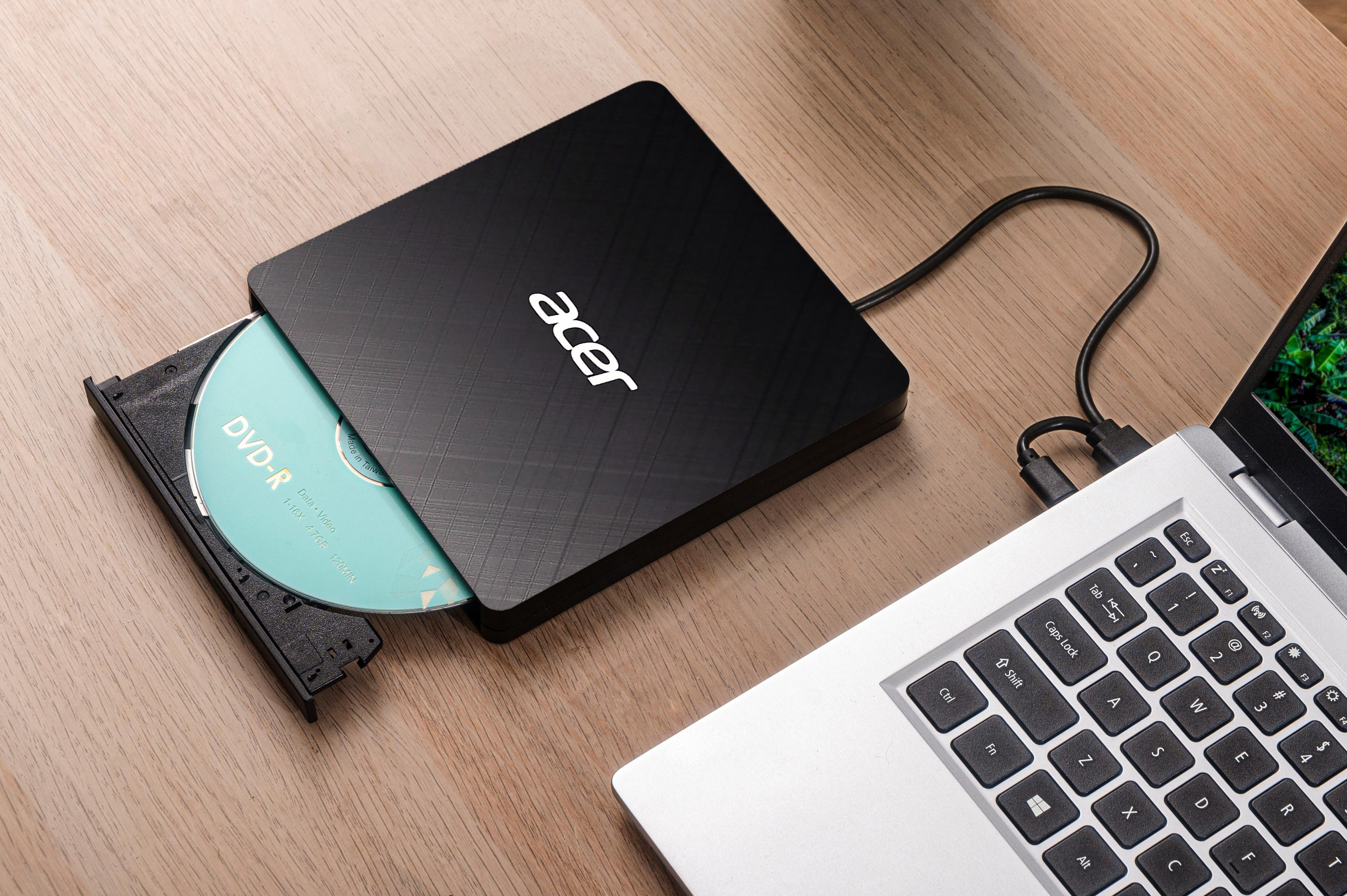 Un masterizzatore DVD Acer nero con un DVD all'interno, collegato a un laptop su una superficie in legno.