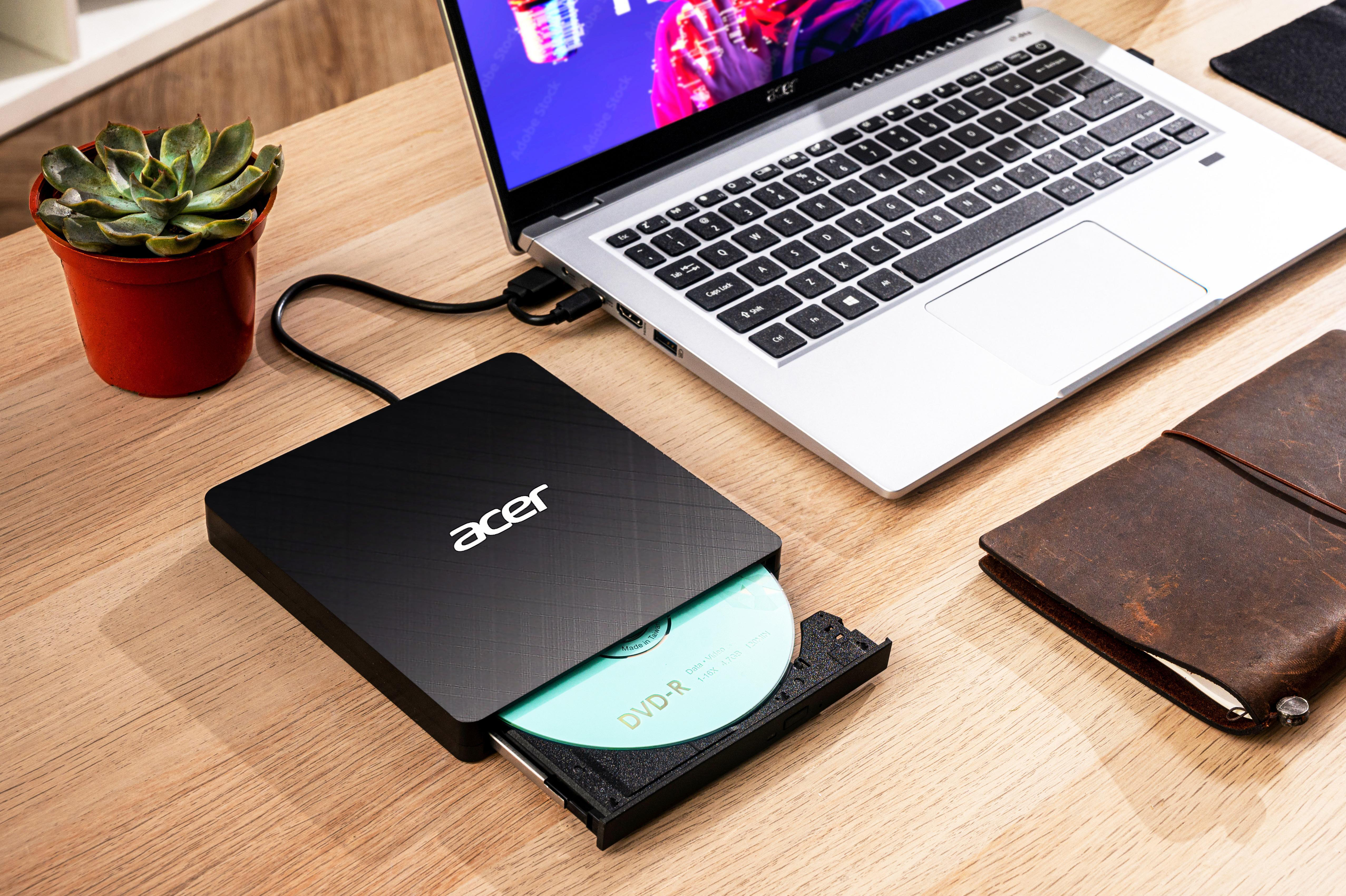 Un laptop, un'unità DVD con disco, un taccuino e una pianta succulenta su un tavolo di legno.