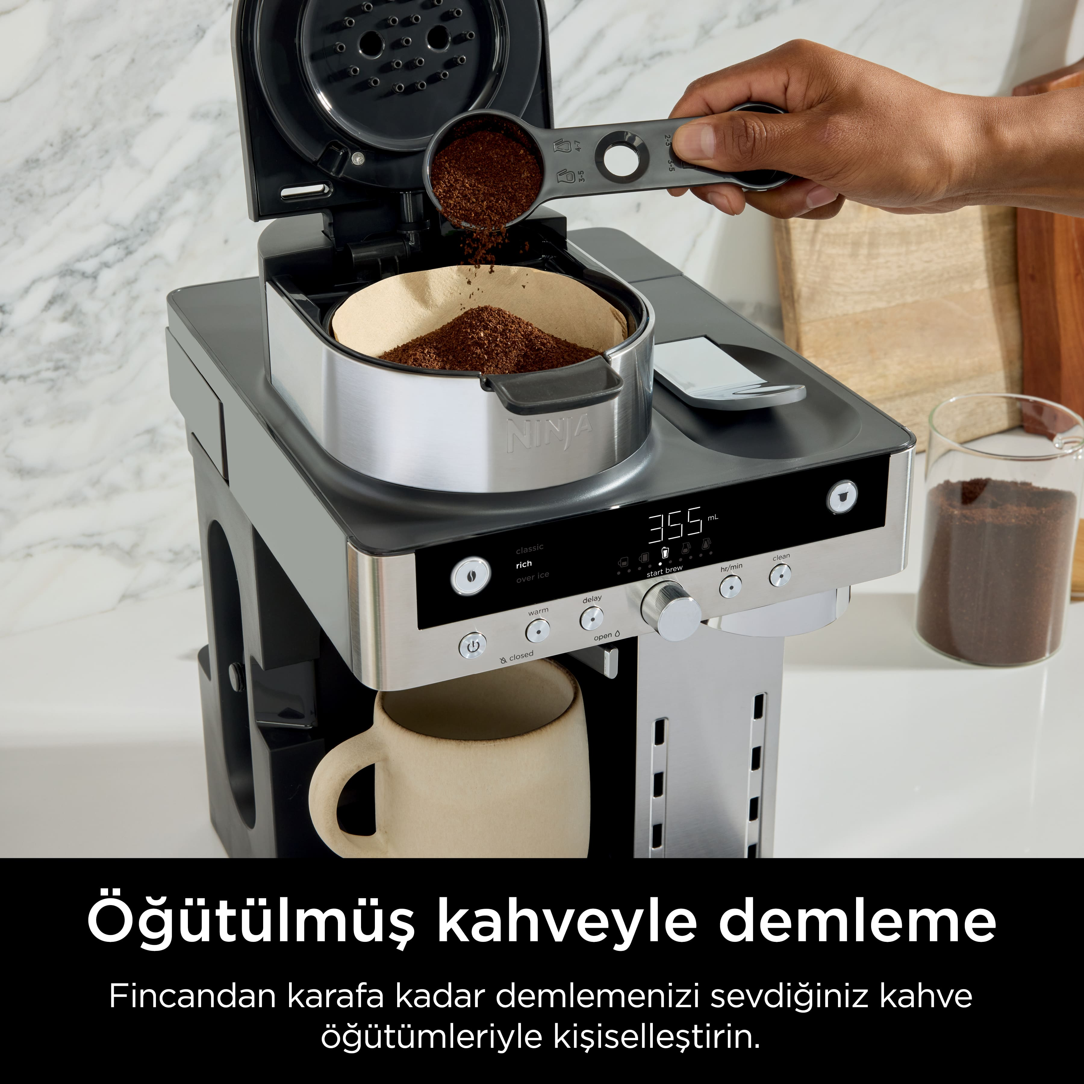 Bir kişi kahve makinesine öğütülmüş kahve döker. Altında bir kupa var. Makinede metin ve yakında bir kavanoz kahve.