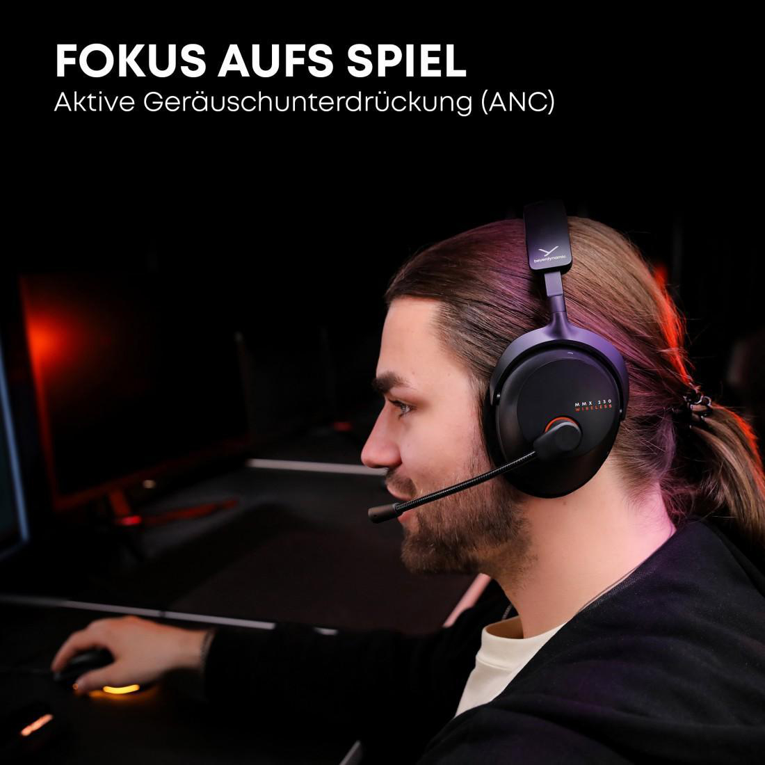 Ein Mann mit Headset und Mikrofon. Er schaut auf einen Computerbildschirm und hält eine Maus. Der Hintergrund ist dunkel.