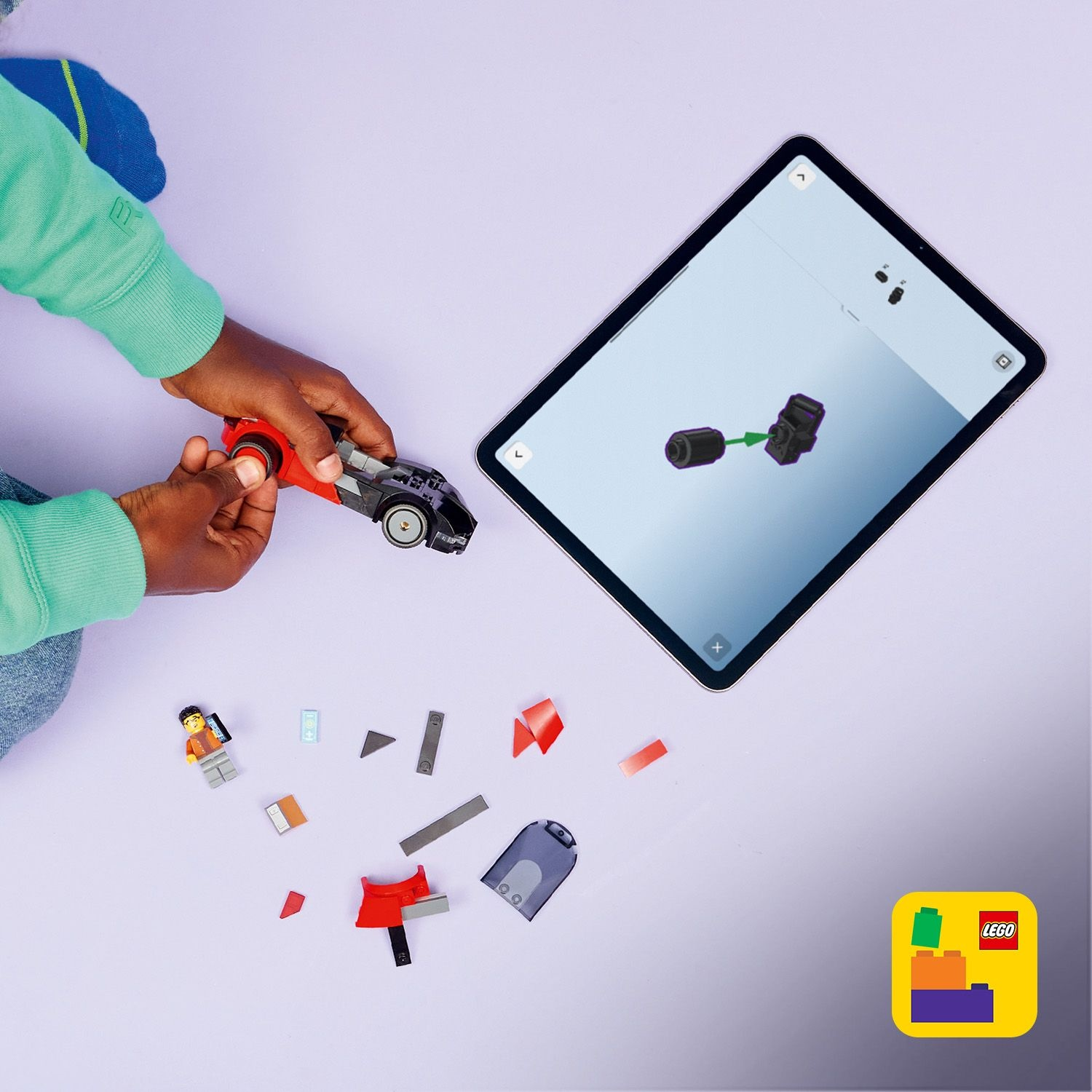 Un bambino assembla un'auto Lego, guidato da un tablet. Pezzi Lego e una minifigure sono sparsi su una superficie viola. Visibile il logo Lego.