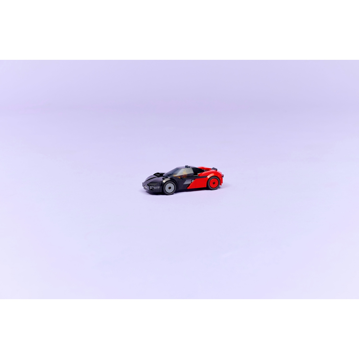 Un'auto giocattolo, nera e rossa, su sfondo lilla chiaro. L'auto è elegante, con ruote visibili, posizionata centralmente.