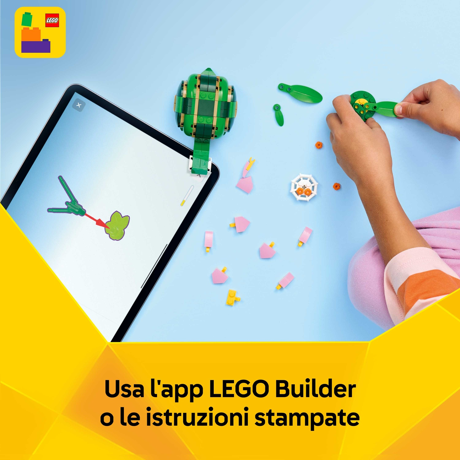Una persona assembla un set Lego verde. Un tablet mostra le istruzioni. Vari pezzi Lego sono sparsi su una superficie blu.