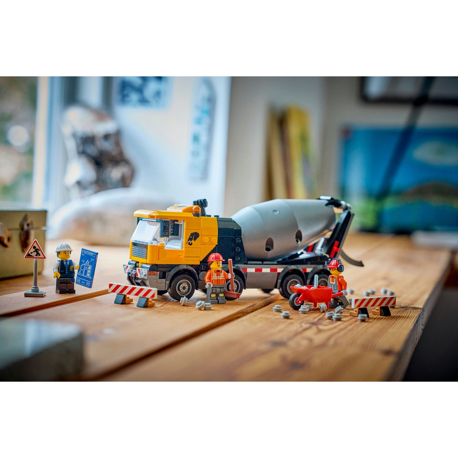 Una scena di costruzione Lego con un camion betoniera, operai, segnali stradali e barriere su una superficie di legno.