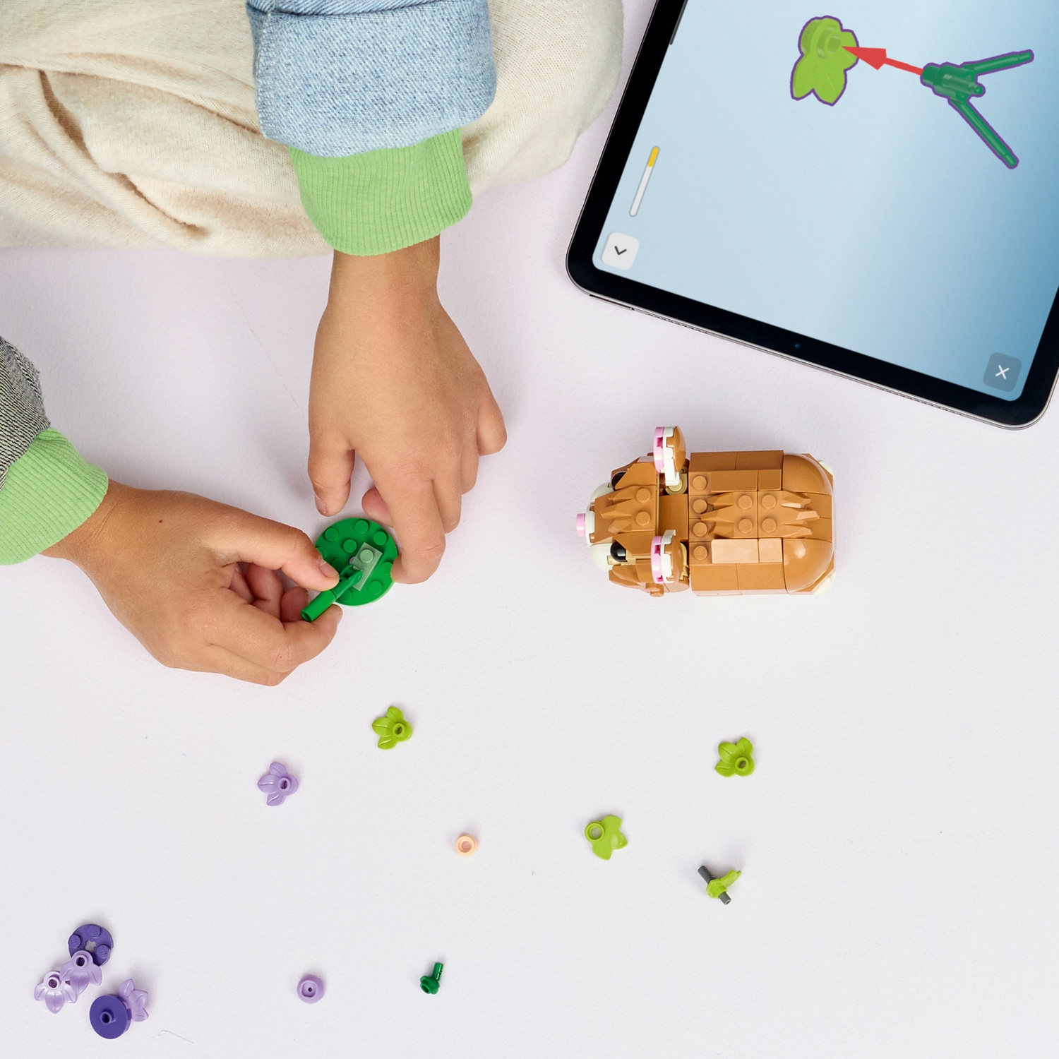 Un bambino assembla un set Lego con un tablet che mostra le istruzioni. Vari pezzi Lego sono sparsi su una superficie bianca.