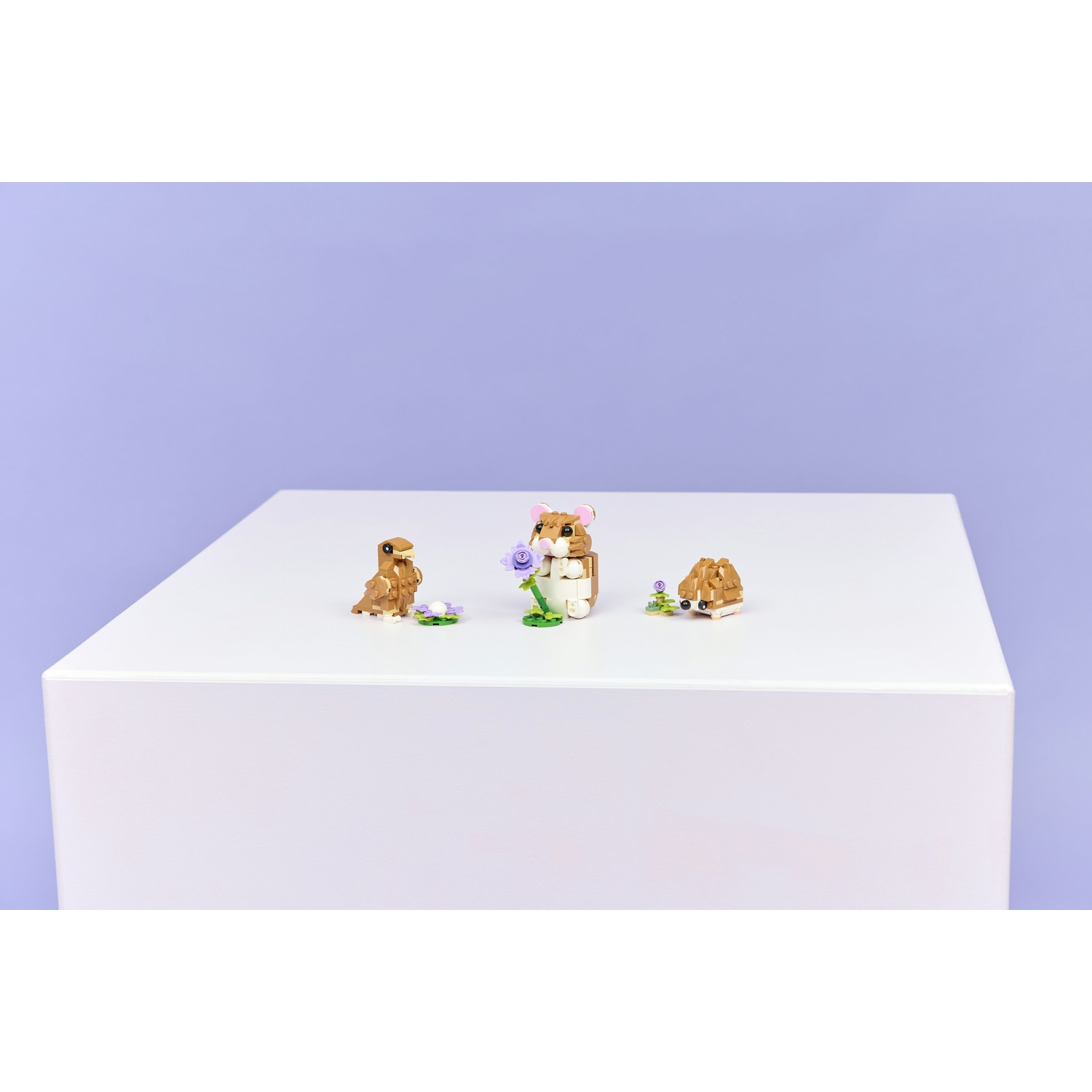 Tre figure di animali Lego su una superficie bianca con sfondo viola. Gli animali includono un criceto, un riccio e un uccello.