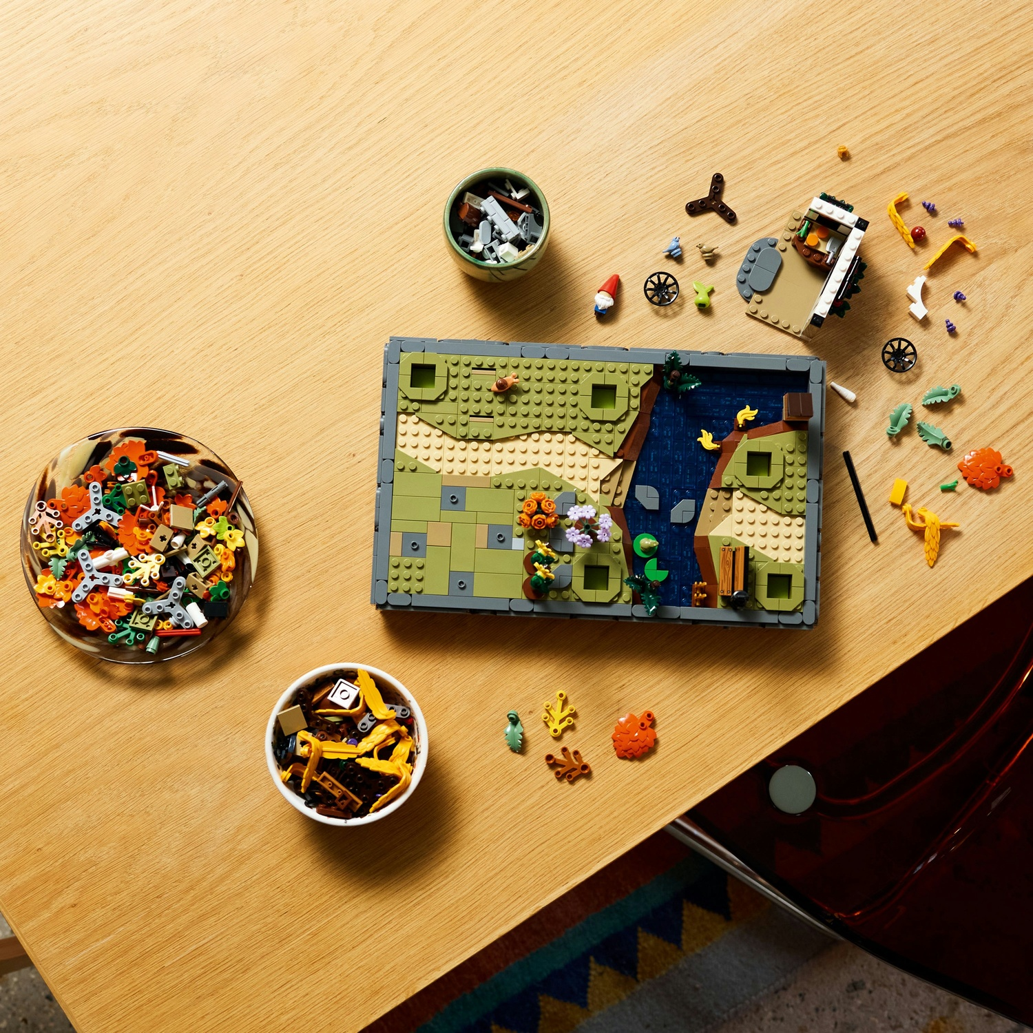 Set Lego su un tavolo di legno. Include un paesaggio, ciotole di pezzi Lego ed elementi sparsi. Sono visibili uno gnomo e delle ruote.