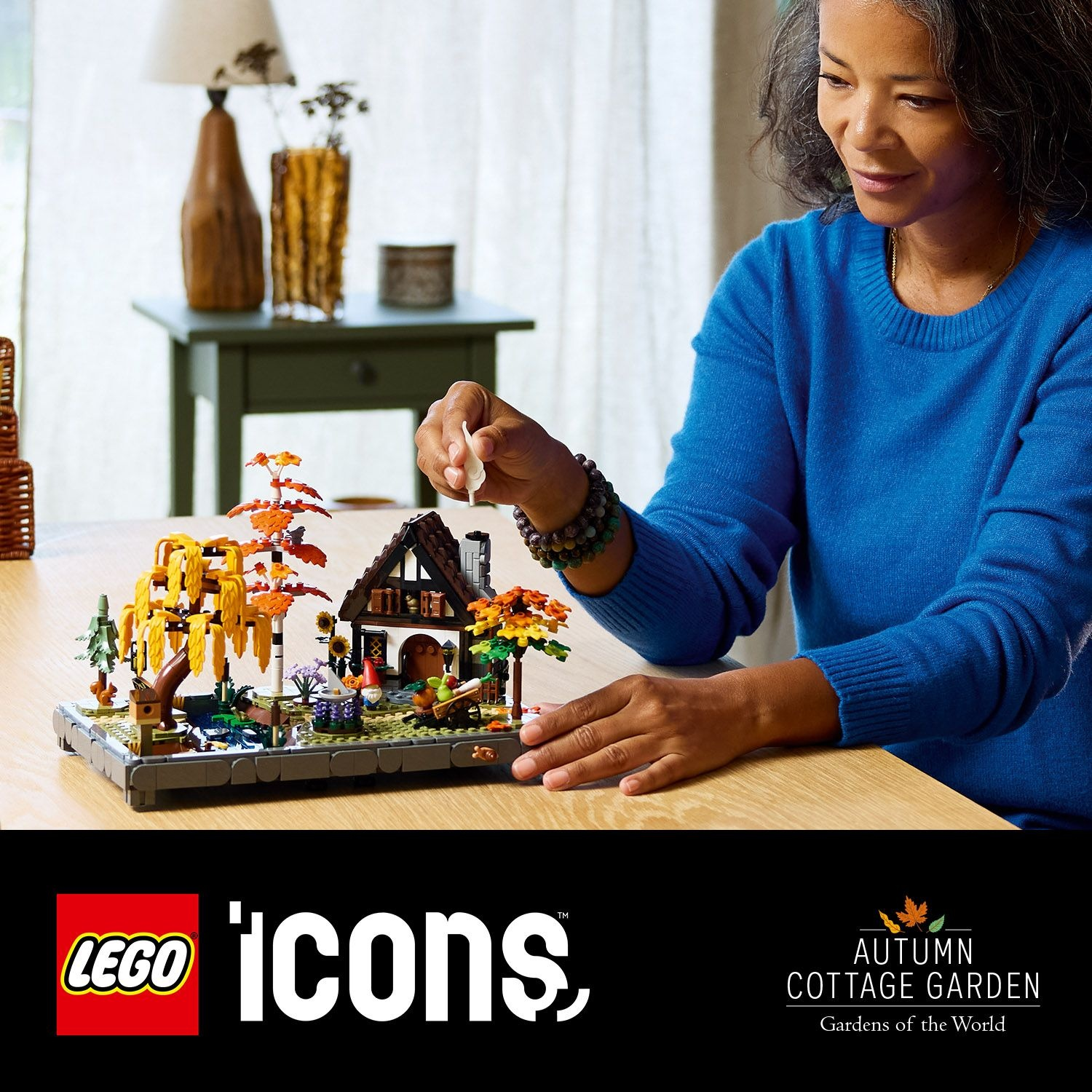 Una donna costruisce un set Lego cottage garden. Il set presenta una casa, alberi e altri elementi del giardino. Il logo è visibile.