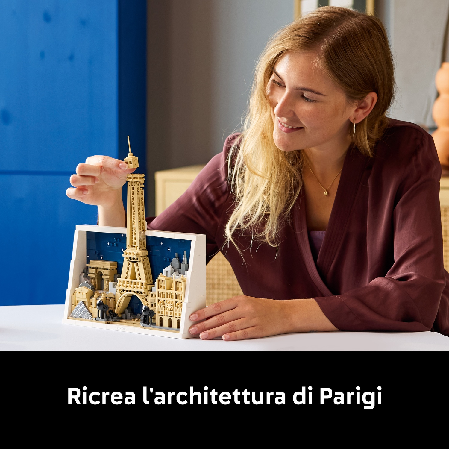 Una donna sorride mentre assembla un modello Lego del paesaggio urbano di Parigi. Il modello presenta la Torre Eiffel, l'Arco di Trionfo e altri edifici.