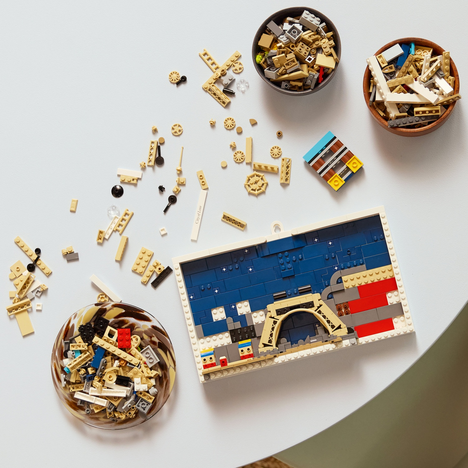 Vista dall'alto di pezzi Lego sparsi su un tavolo bianco. Ciotole contengono pezzi e una costruzione Lego di un ponte è parzialmente assemblata.