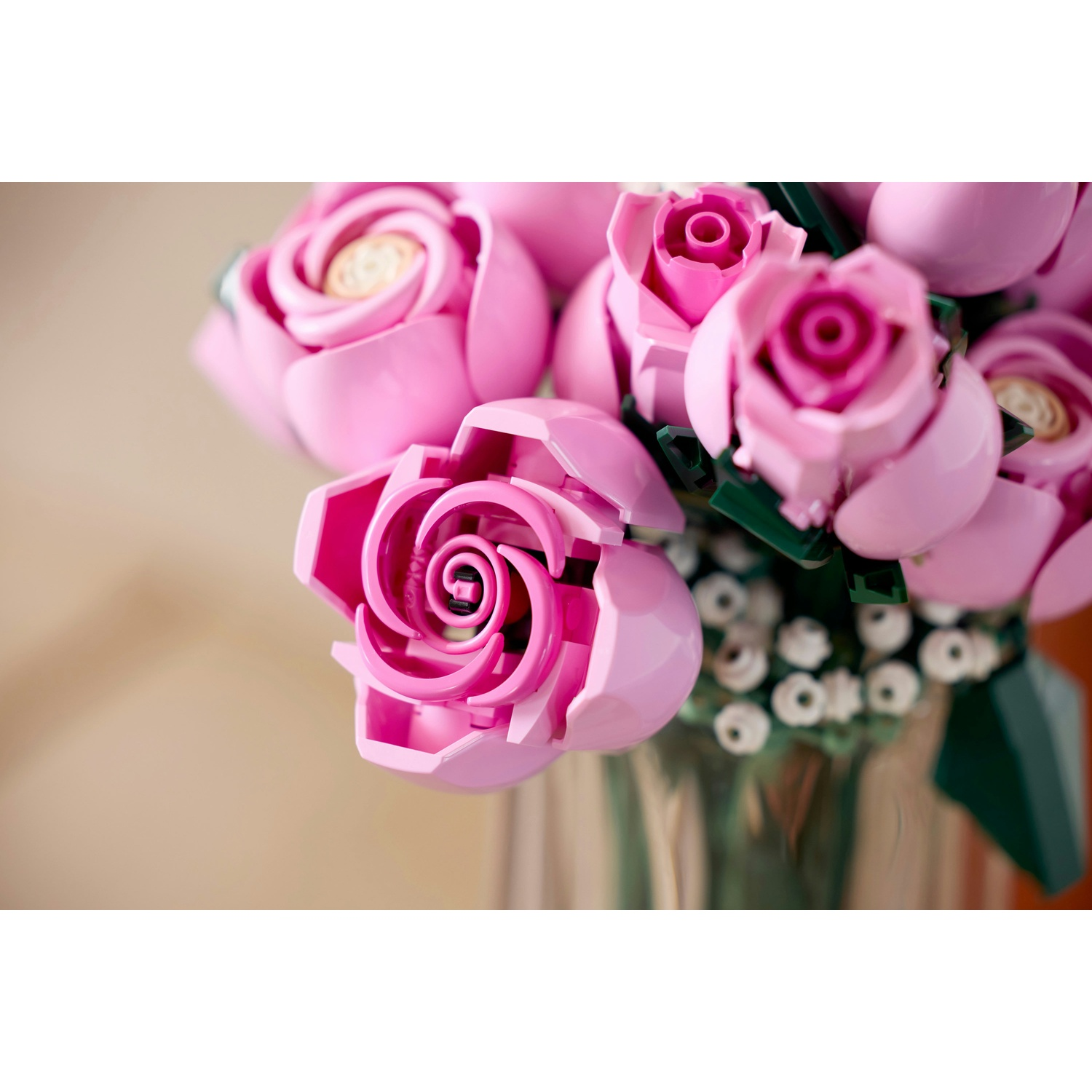 Un primo piano di un bouquet di rose rosa in un vaso di vetro. Le rose sono di plastica e hanno un design dettagliato.