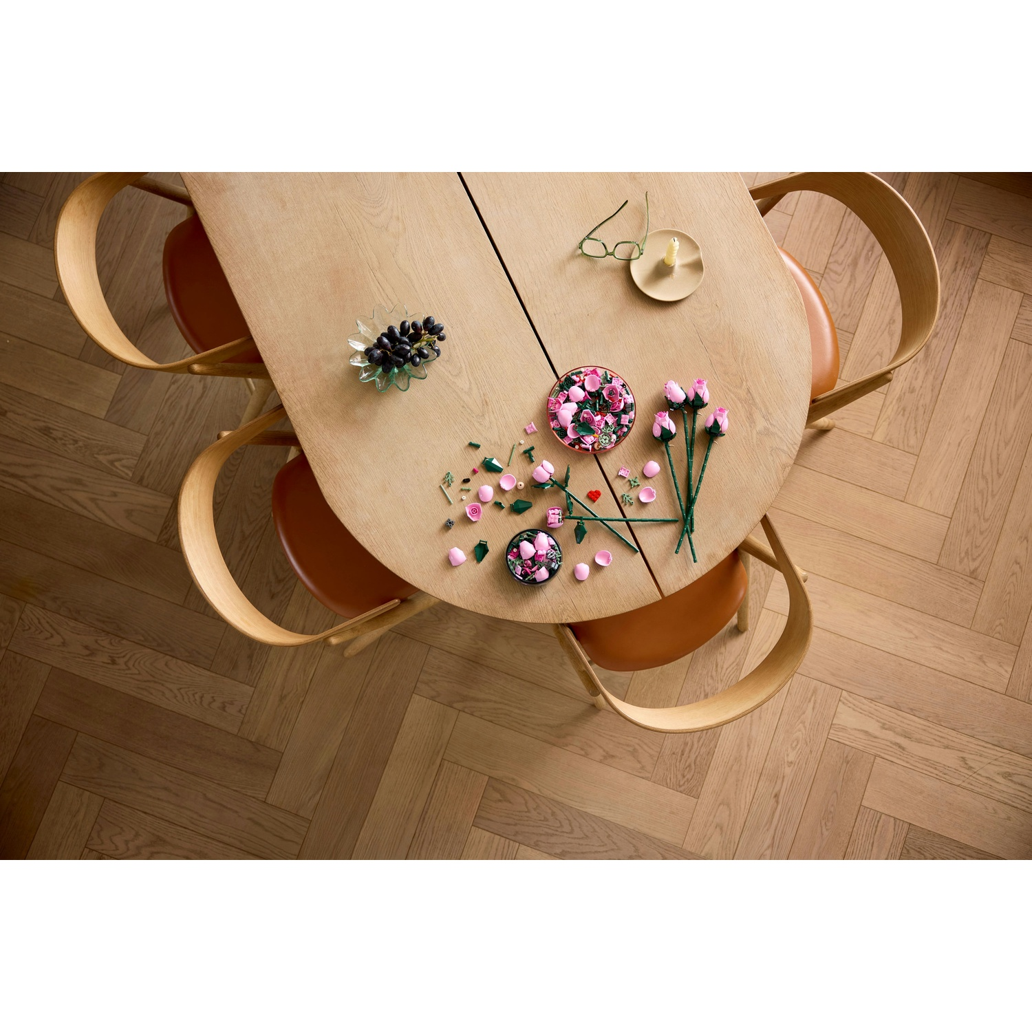 Tavolo in legno con fiori, uva e occhiali. Quattro sedie circondano il tavolo. Pavimento in legno a spina di pesce.