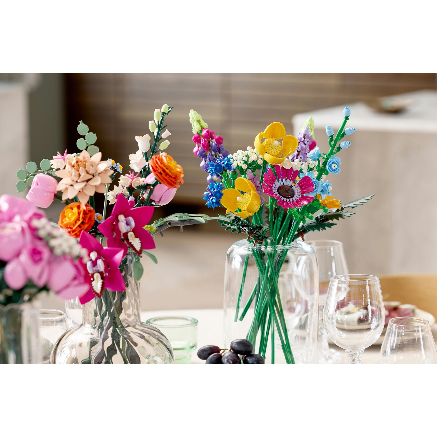 Fiori Lego colorati in vasi con bicchieri e uva su un tavolo. Lo sfondo mostra un'area pranzo sfocata.