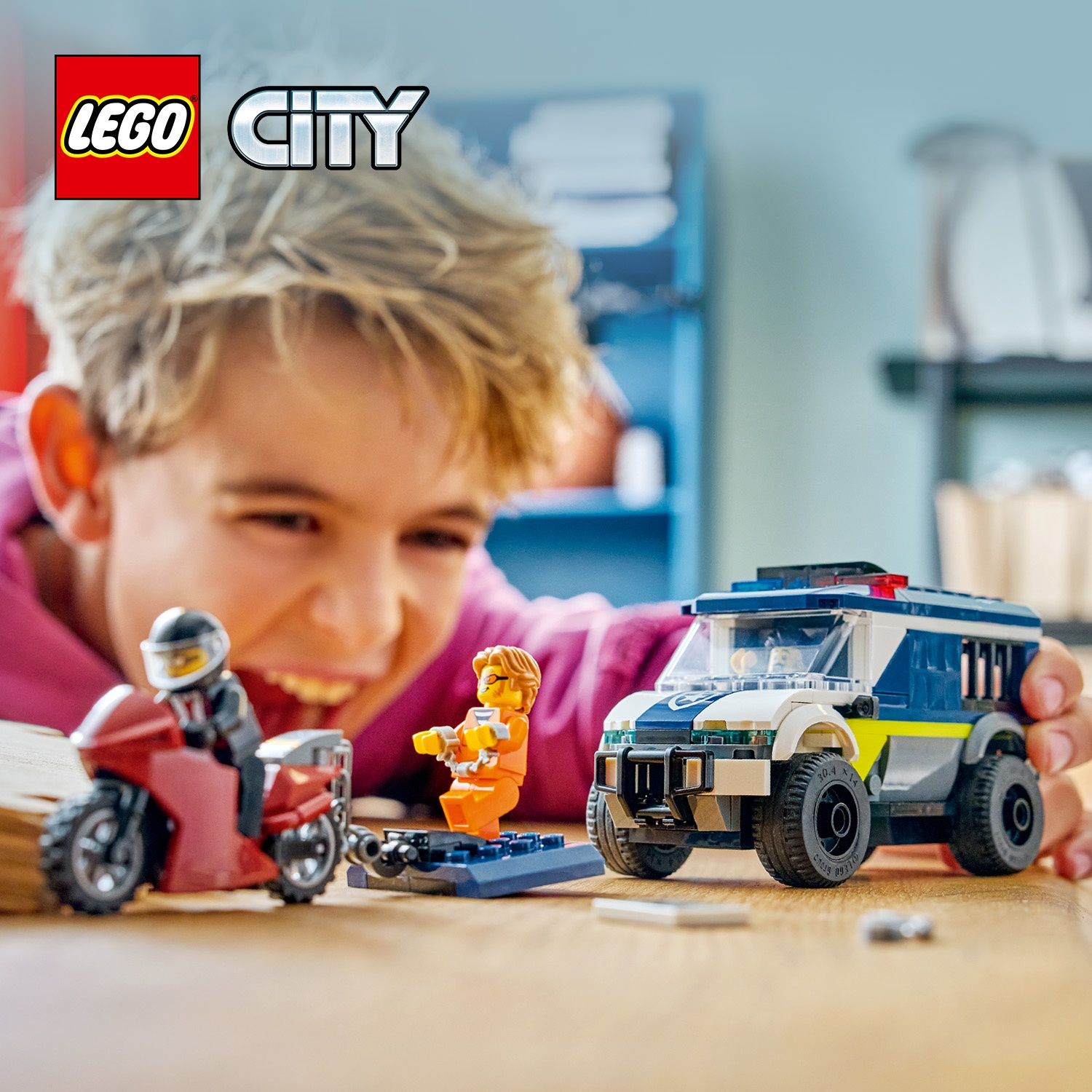 Un bambino sorride a un set LEGO City con un furgone della polizia, una moto e le minifigure di un prigioniero e un agente.