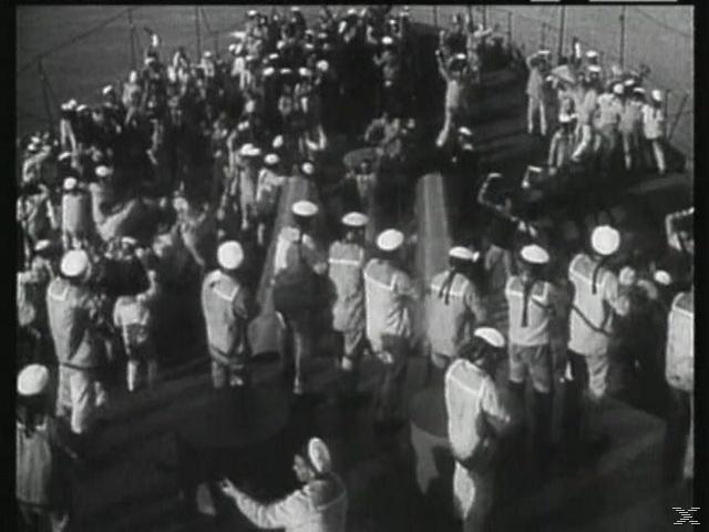 Viele Seeleute in Uniform auf dem Schiffsdeck. Einige winken. Die meisten tragen weiße Hüte. Schwarz-Weiß-Bild.