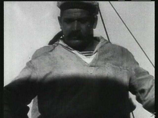 Ein Mann mit Schnurrbart trägt Matrosenmütze und Hemd. Das Bild ist schwarzweiß, wahrscheinlich aus einem älteren Film.