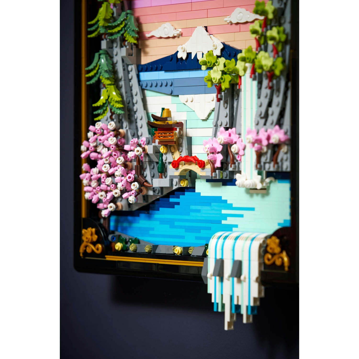 Un diorama Lego presenta una scena di montagna con una cascata, alberi e un ponte. I colori includono blu, rosa, verde e bianco.