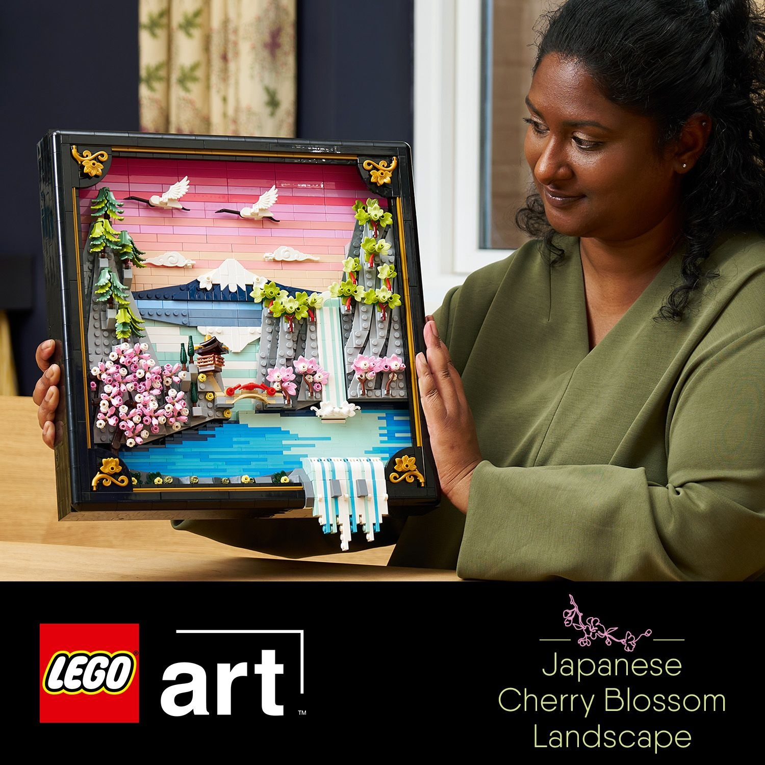 Donna che tiene un Lego Paesaggio di fiori di ciliegio giapponesi. Presenta una montagna, acqua, fiori e uccelli in una cornice nera.