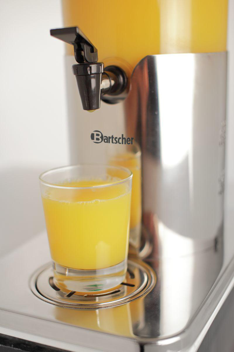 Ein klares Glas Orangensaft steht auf einem silbernen Tablett. Hinter dem Glas befindet sich ein Saftspender mit schwarzem Hahn.
