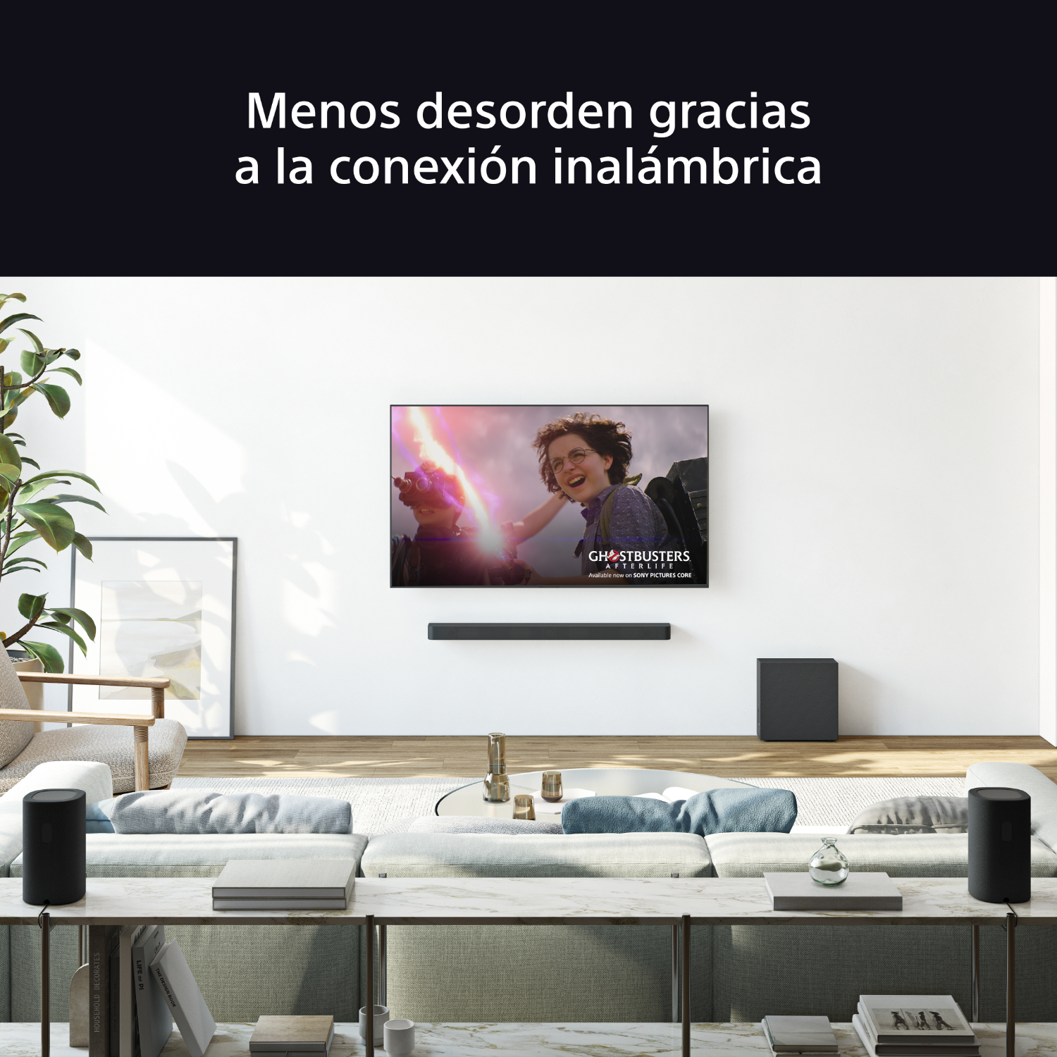 Salón con TV mostrando Cazafantasmas, sistema de sonido, sofá, mesa de centro y libros. Paredes blancas y suelo de madera.