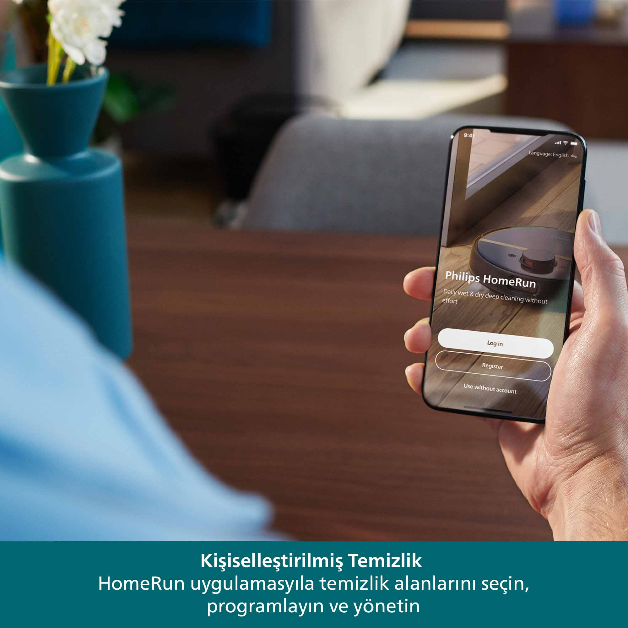 Elde Philips HomeRun uygulaması arayüzünü gösteren bir telefon tutuluyor. Arka planda vazoda çiçekler var.