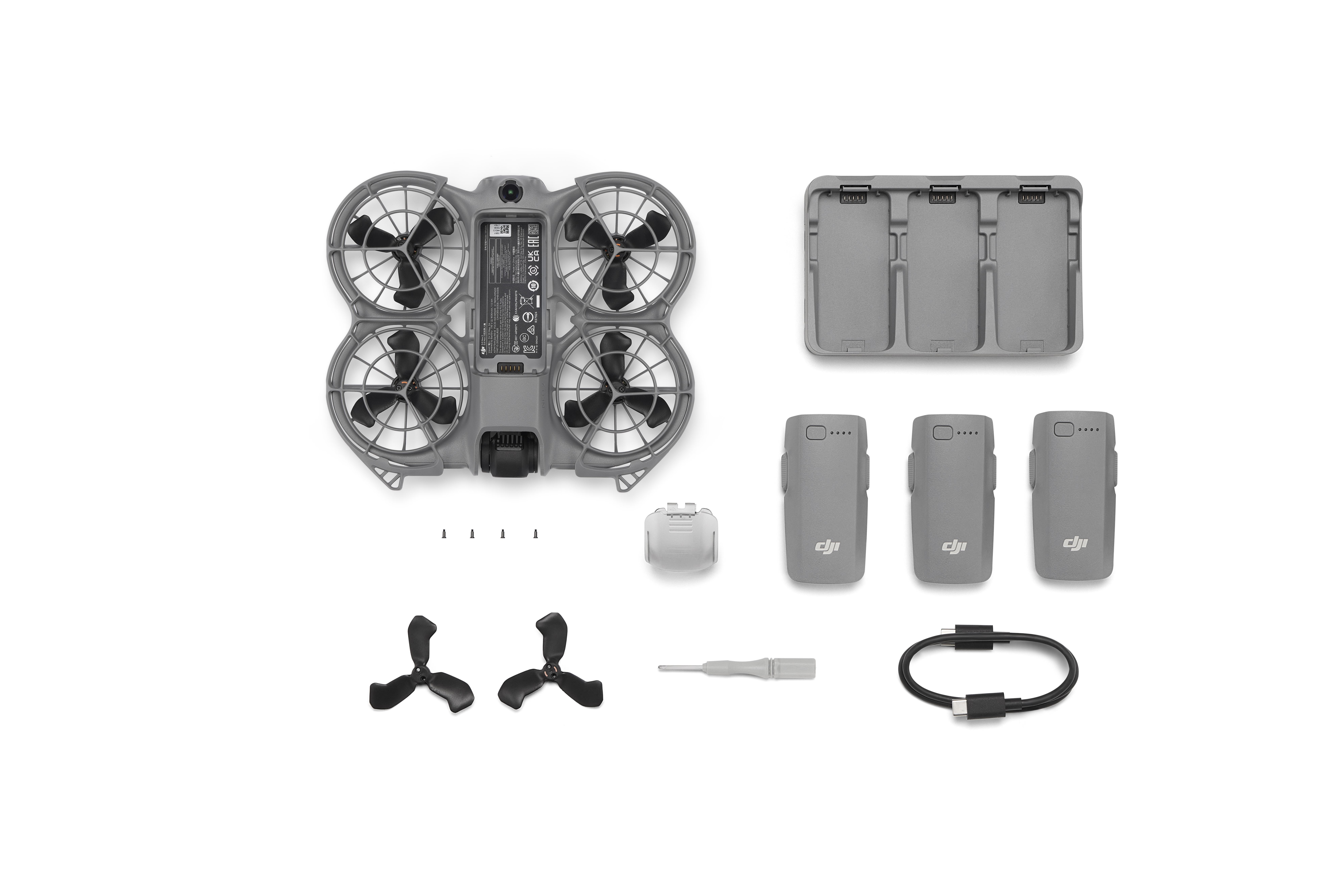 Drone ve aksesuarları. Drone sol üstte. Piller, şarj cihazı, pervaneler, tornavida ve USB-C kablosu.